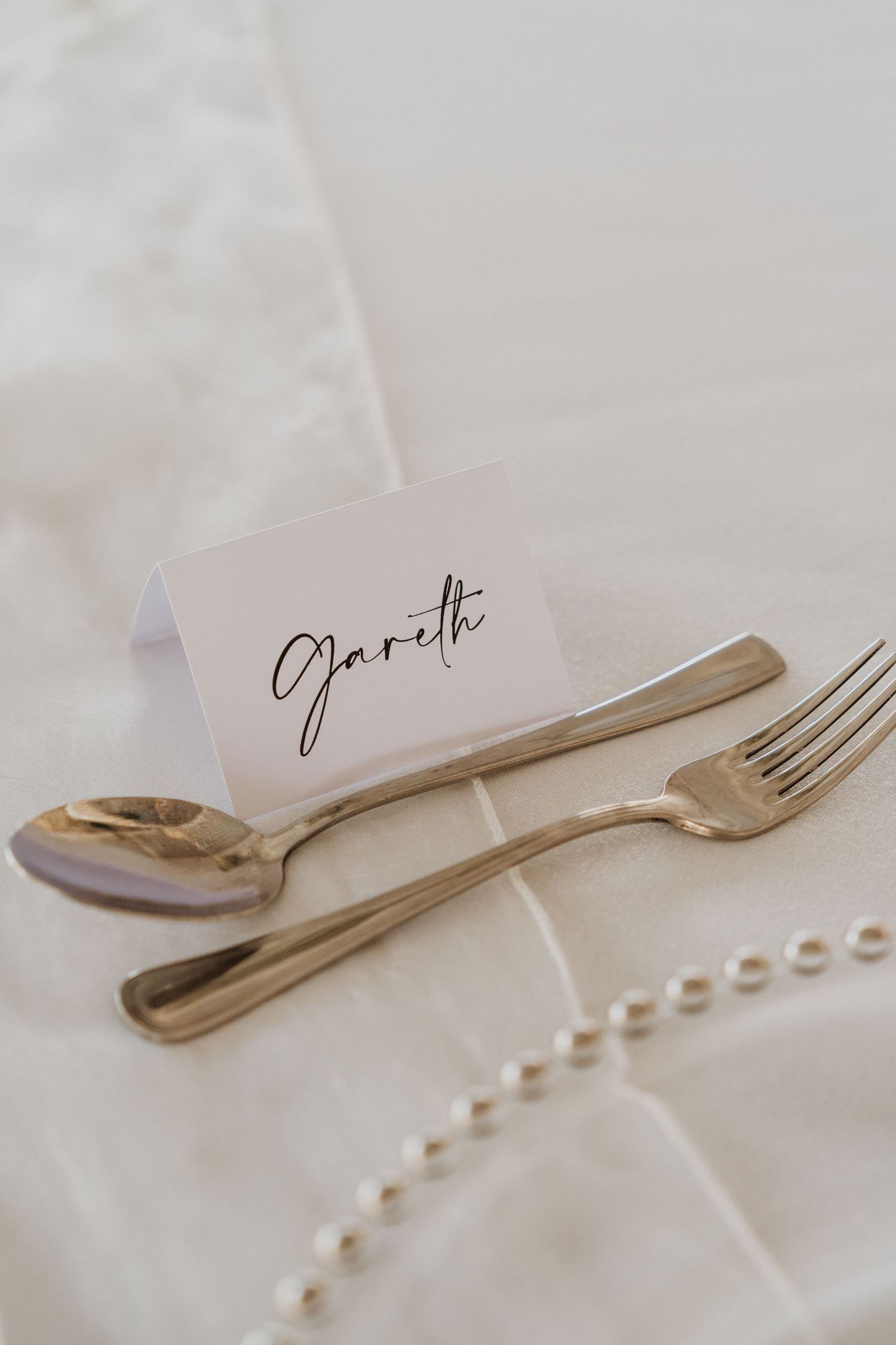 Elegant place setting with silver cutlery and handwritten name card on white linen.