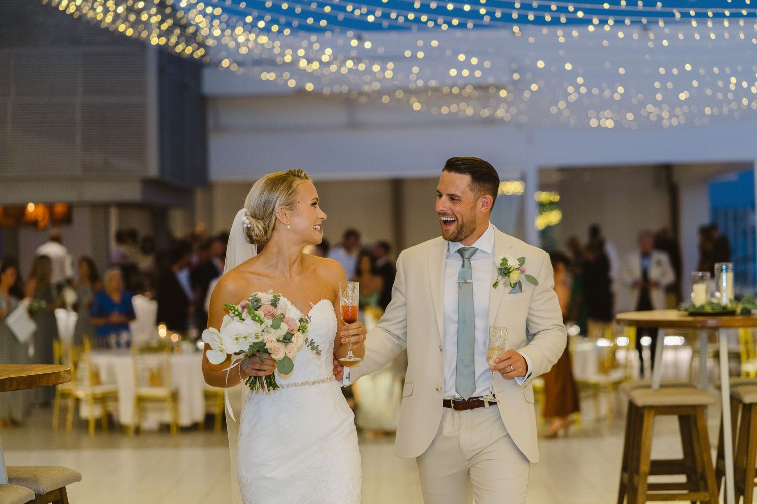 Bride and groom laugh together while holding champagne during their wedding reception.