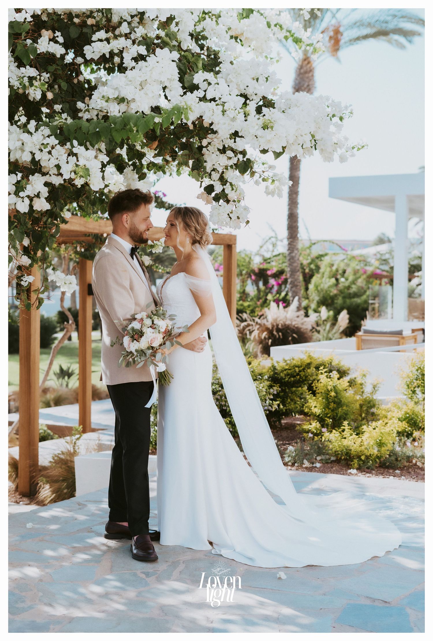 Couple shares an intimate moment under flowering trees in a garden wedding setting.