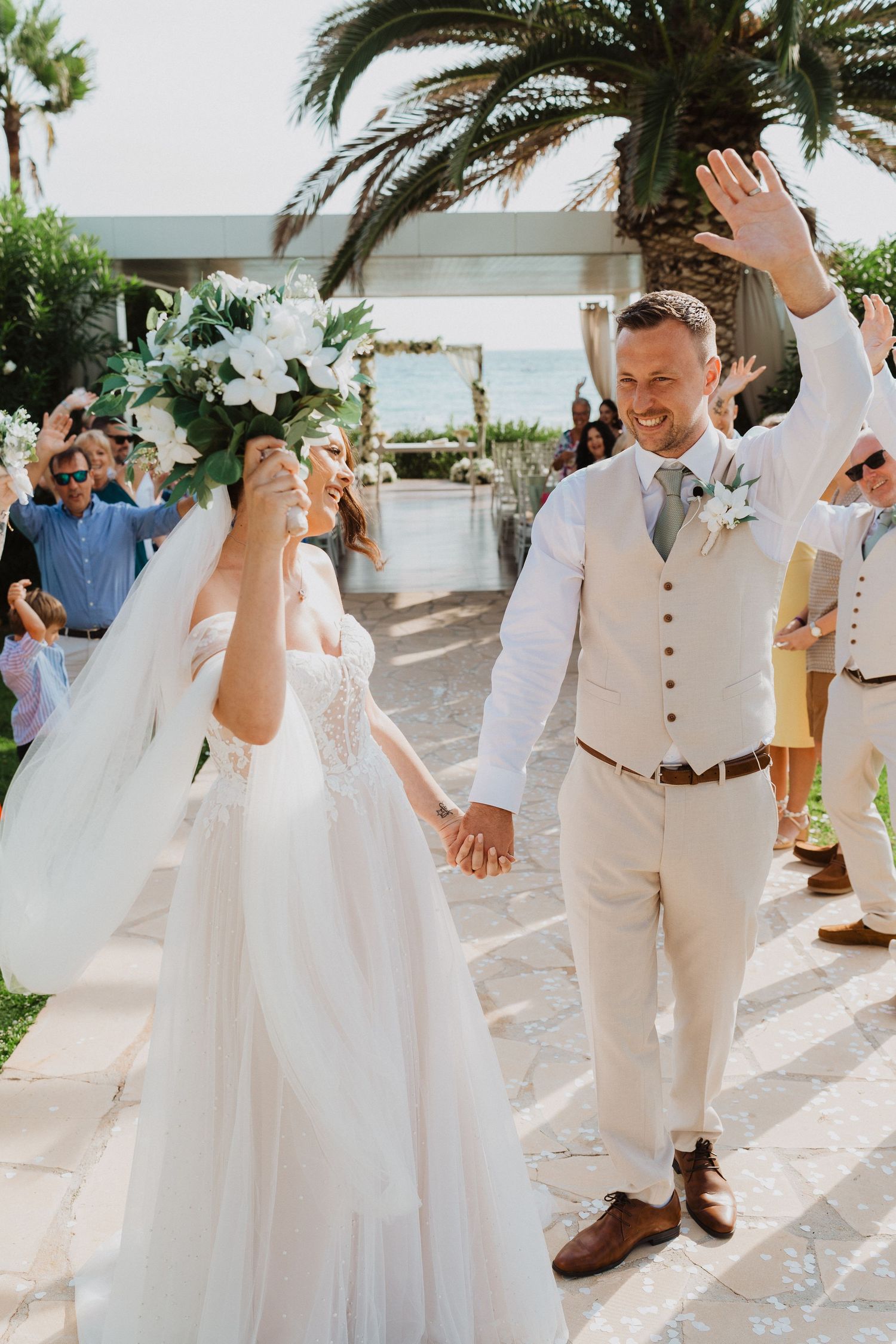 A joyful wedding celebration at a tropical outdoor venue with palm trees and white floral decorations.