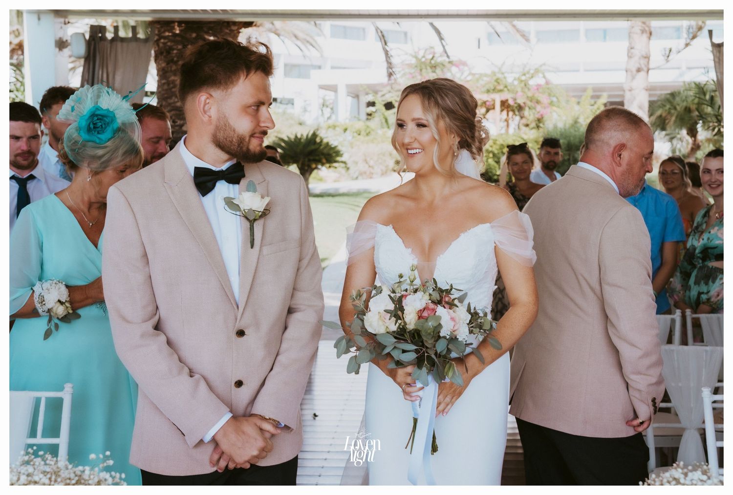 A couple sharing a joyful moment during an outdoor wedding ceremony under a white tent with floral bouquet.