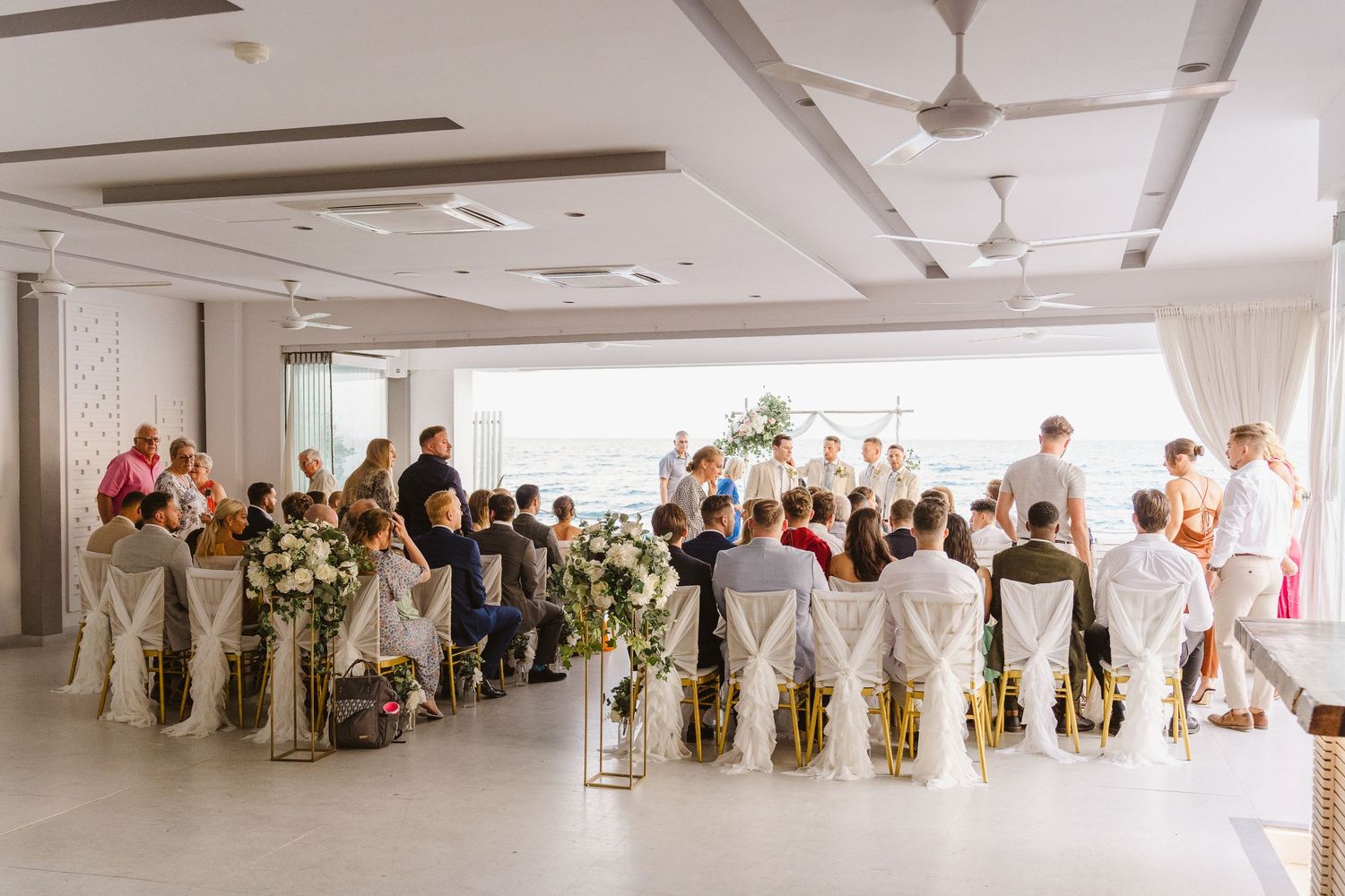 Indoor wedding ceremony setup with white chairs and floral decorations in a modern venue.