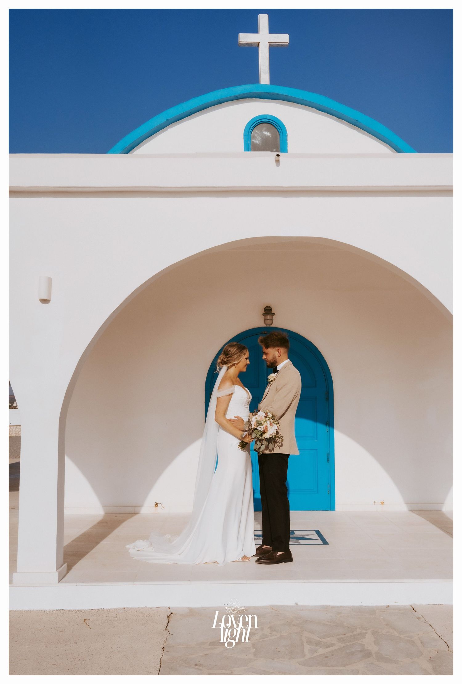 Wedding portrait under white church archway with bright blue door and cross above.