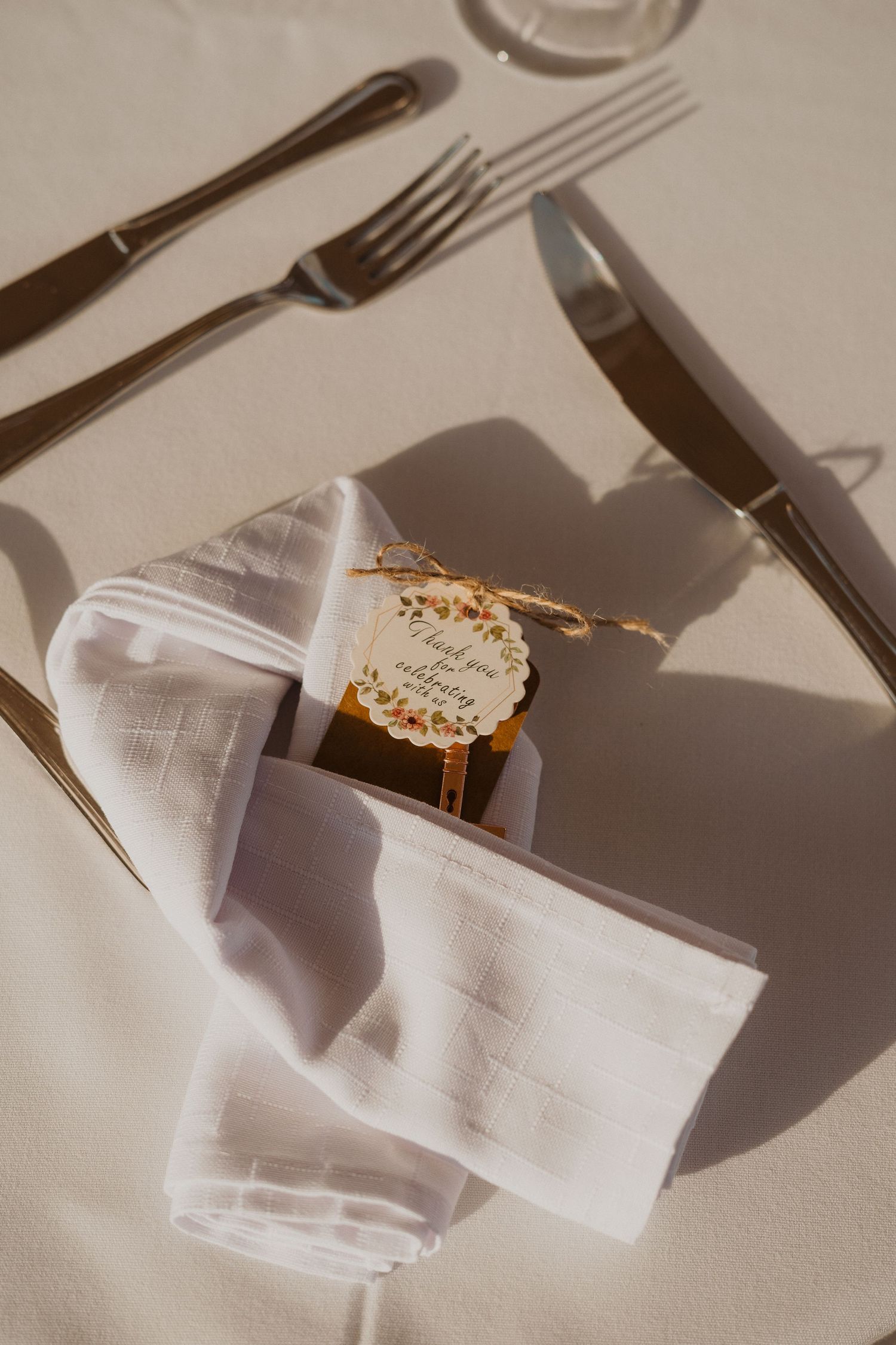 Place setting with white napkin, silverware and place card in sunlit reception setting.