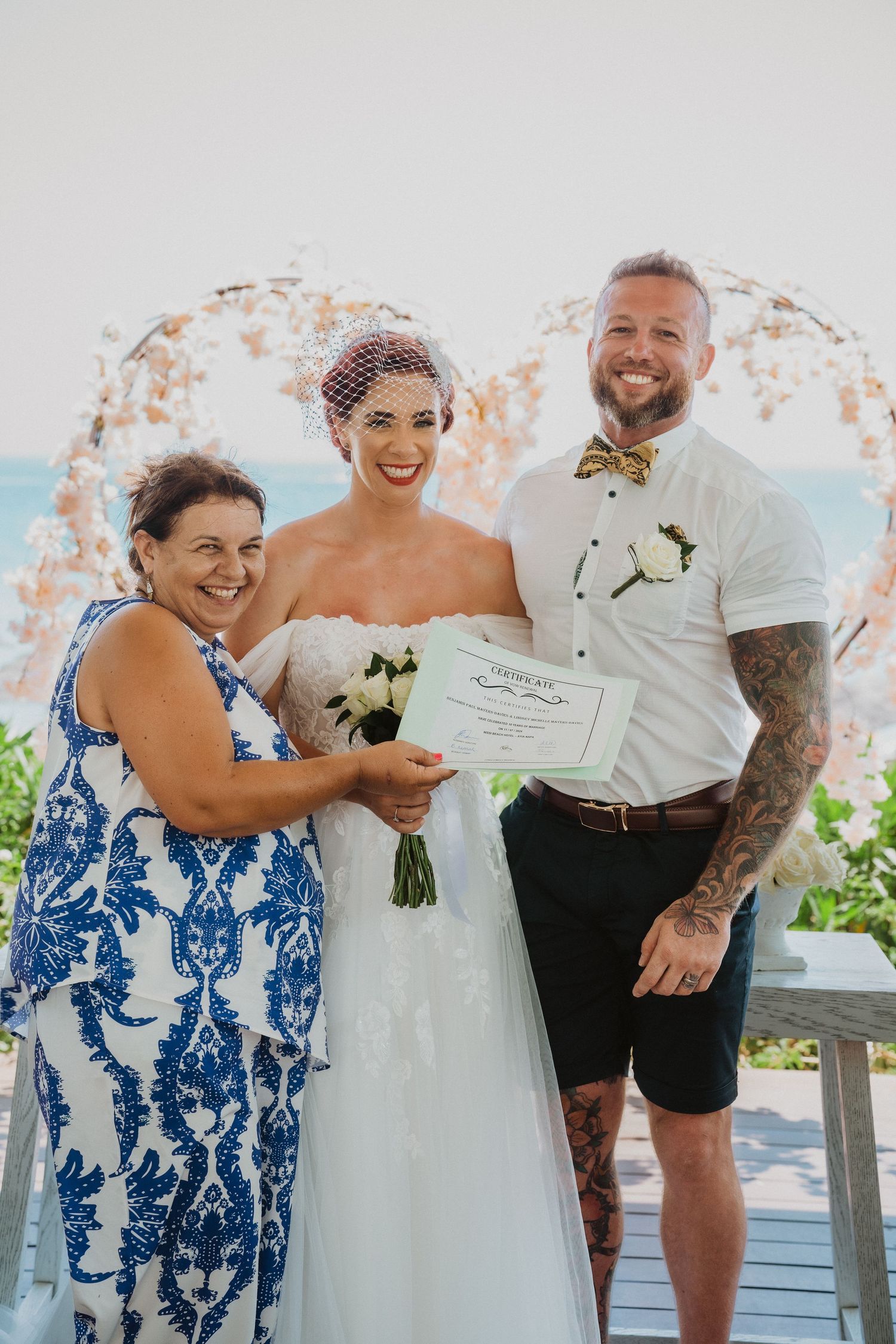 A joyful wedding portrait showing marriage certificate signing with ocean view backdrop.