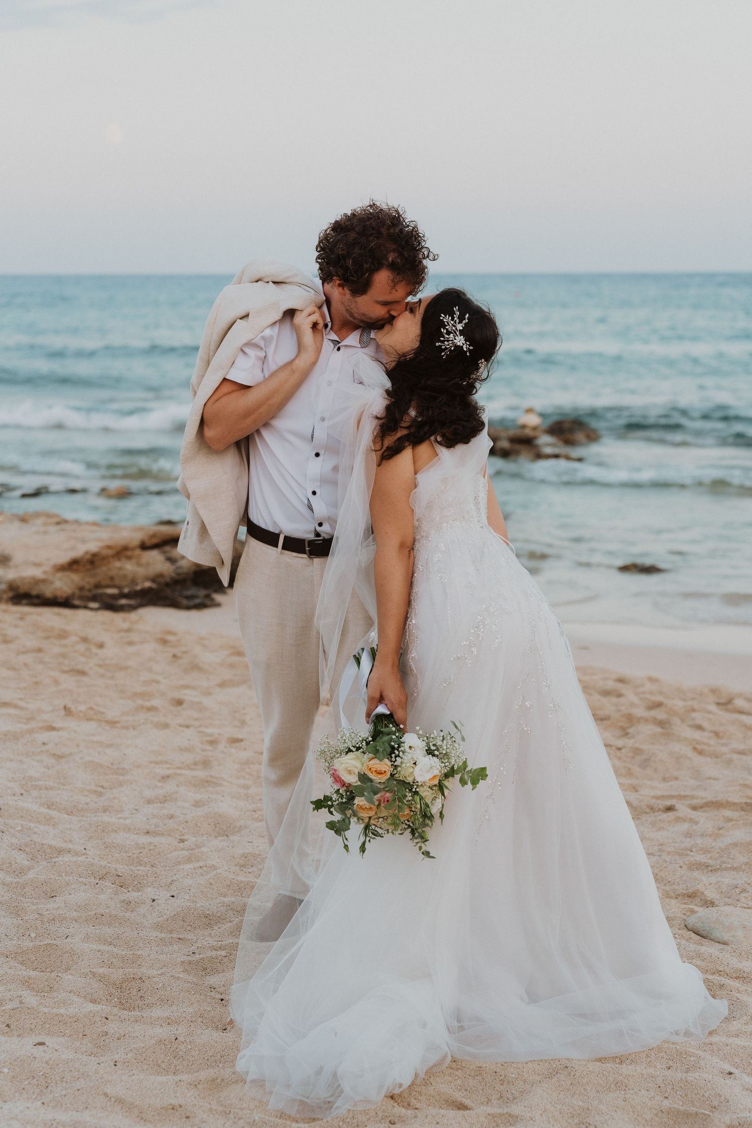 A tender moment between newlyweds on a rocky beach with waves crashing in the background.