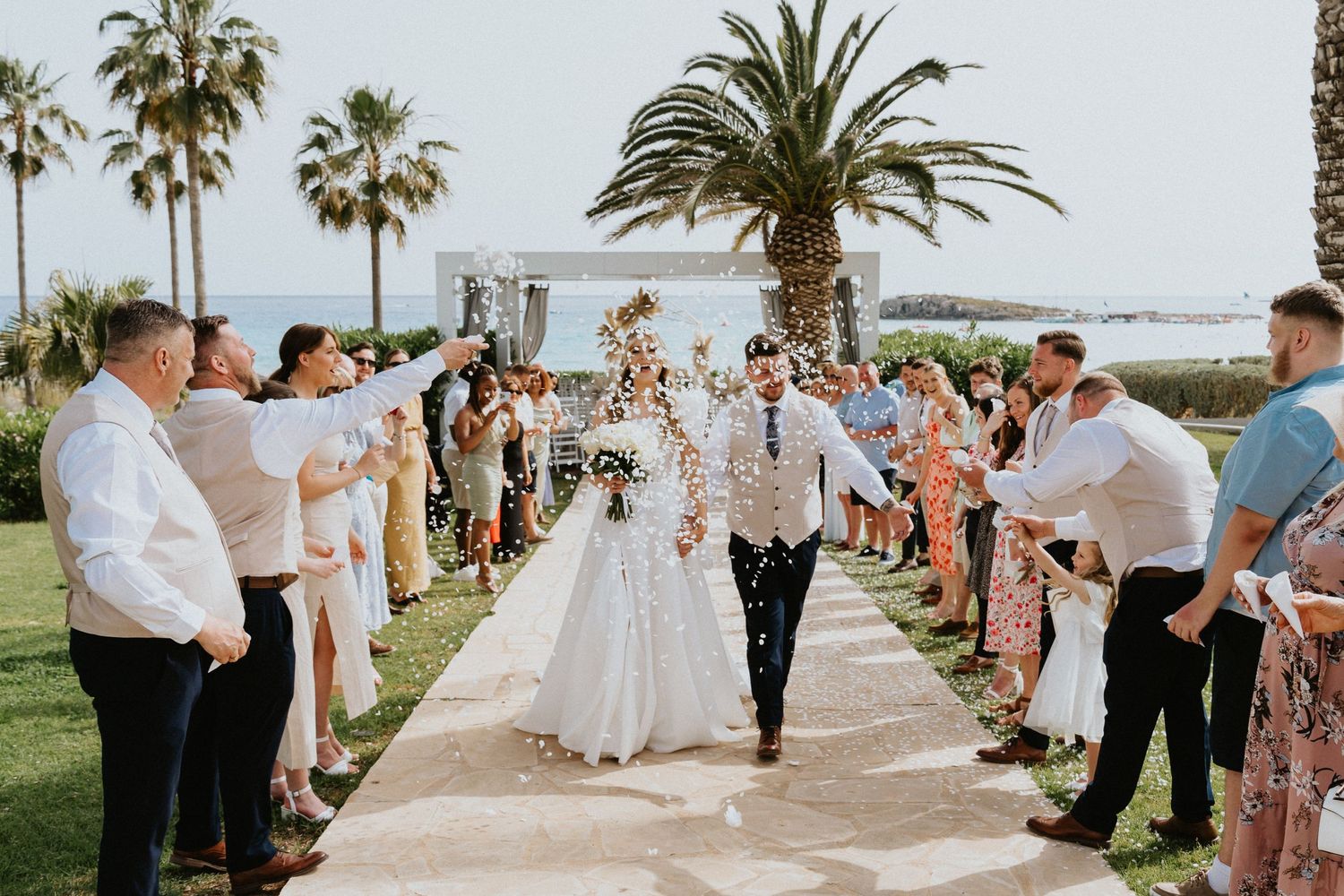 Joyous wedding celebration with guests lining outdoor pathway with palm trees and ocean view.