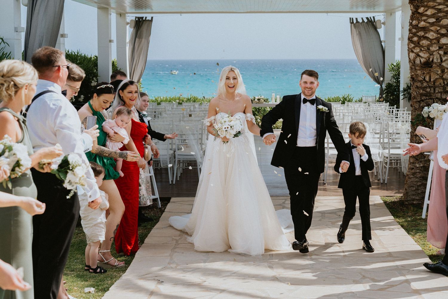Wedding guests line the aisle as newlyweds make their grand exit under a white canopy.