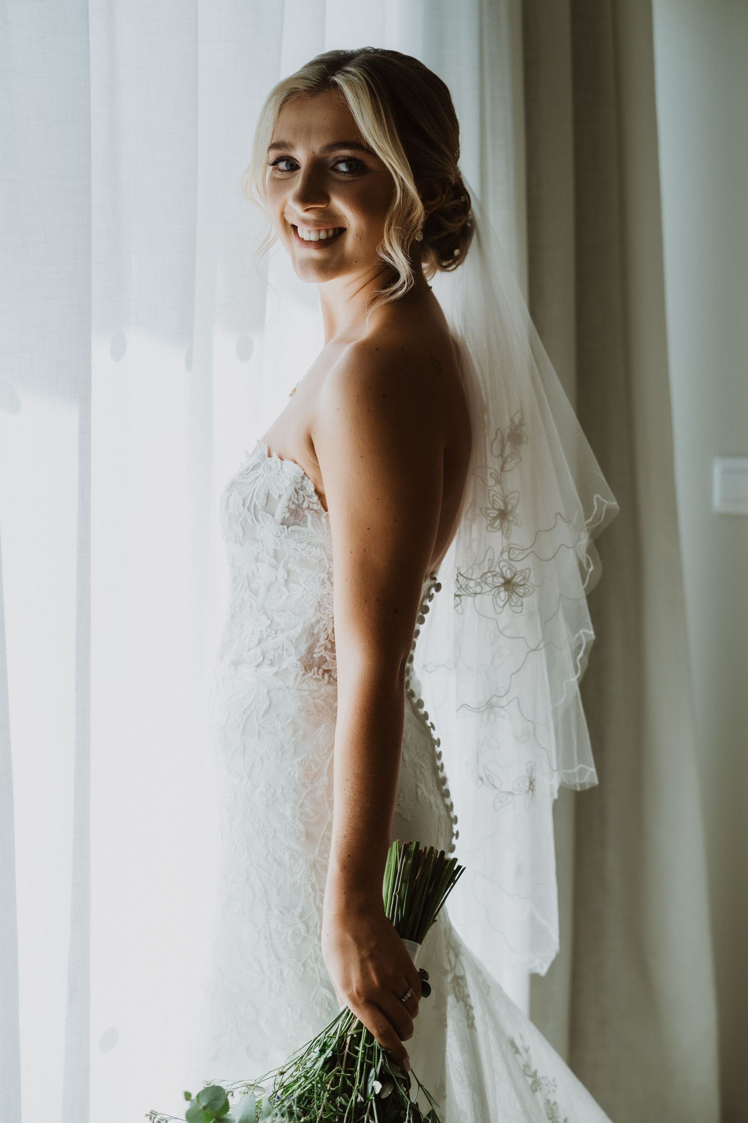 Stunning lace wedding dress with sheer details and flowing veil in natural window light.