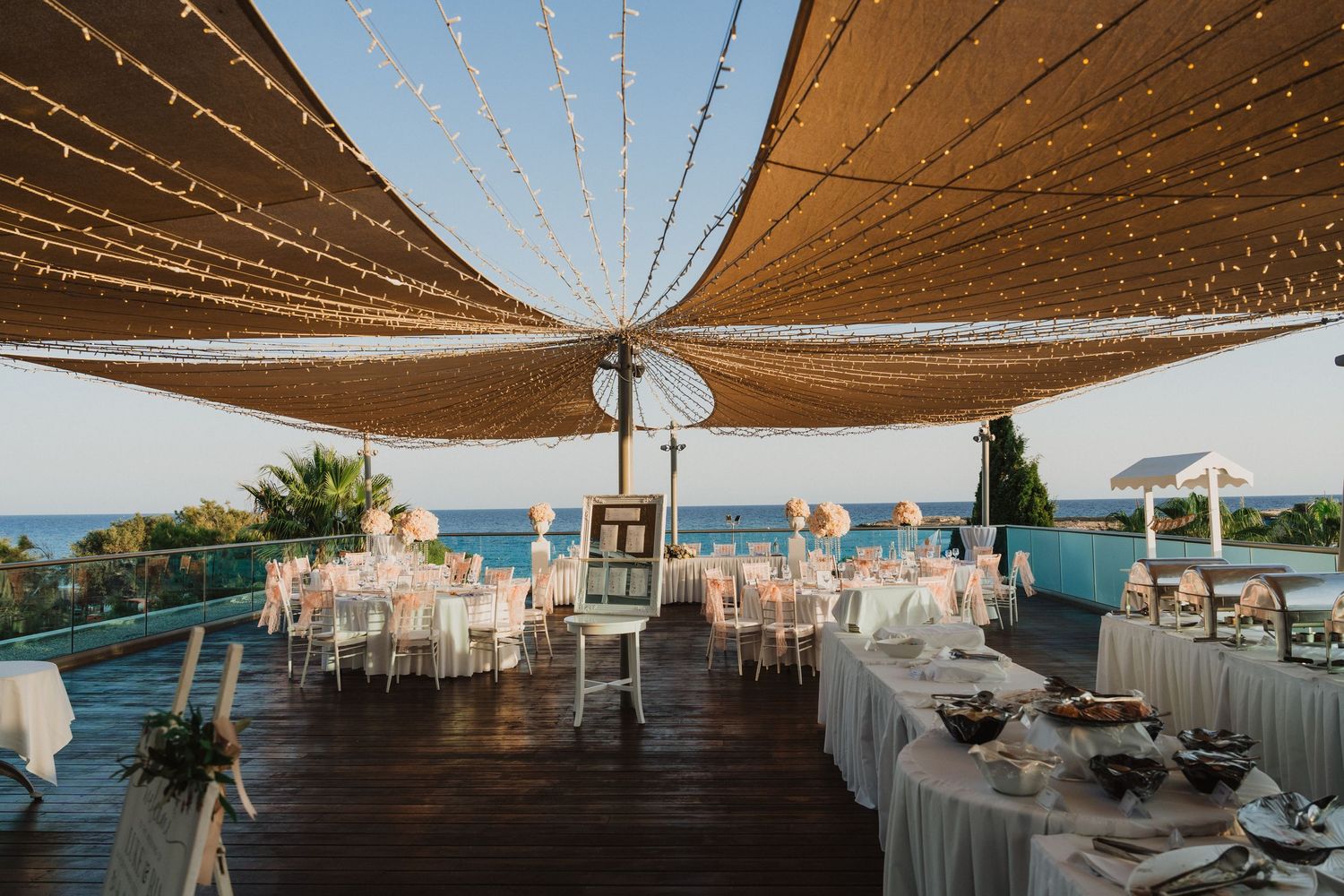 Outdoor wedding reception venue with string lights and brown sail shades overlooking the ocean.