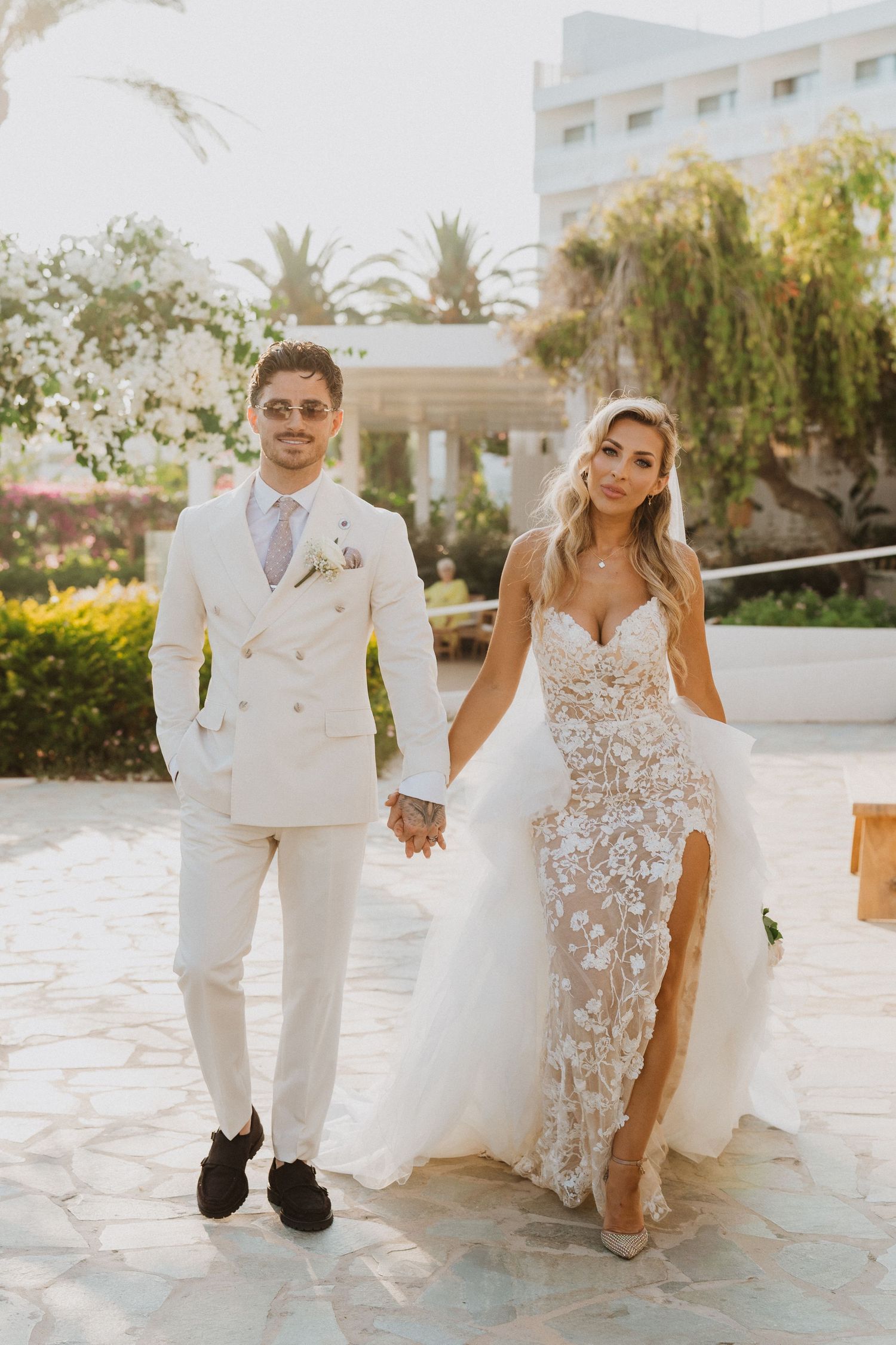 Newlyweds share a joyful moment together on a sunlit stone patio surrounded by lush greenery and palm trees.