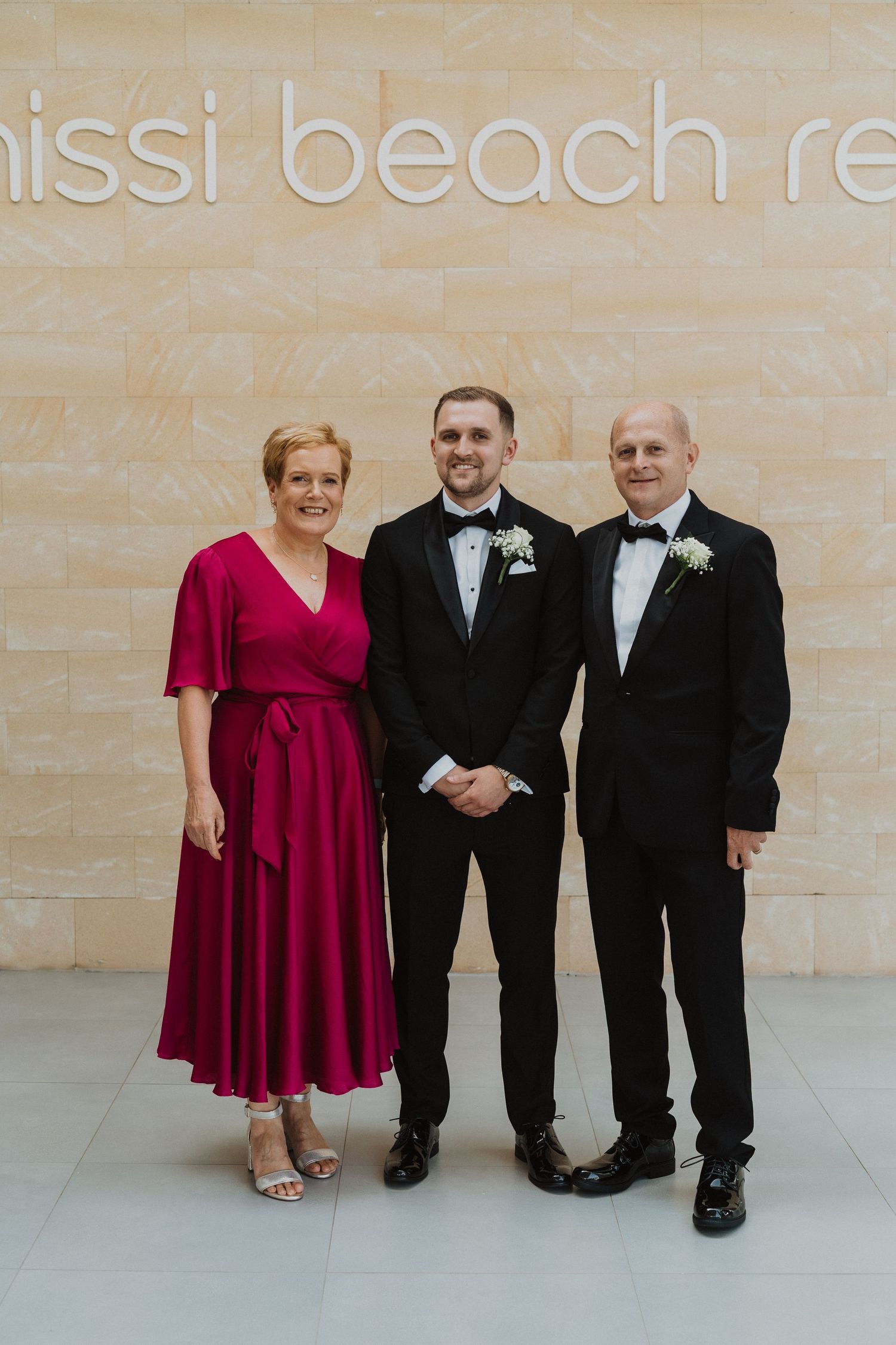 Groom in black tuxedo poses with parents at Mississauga Beach Resort wedding venue.