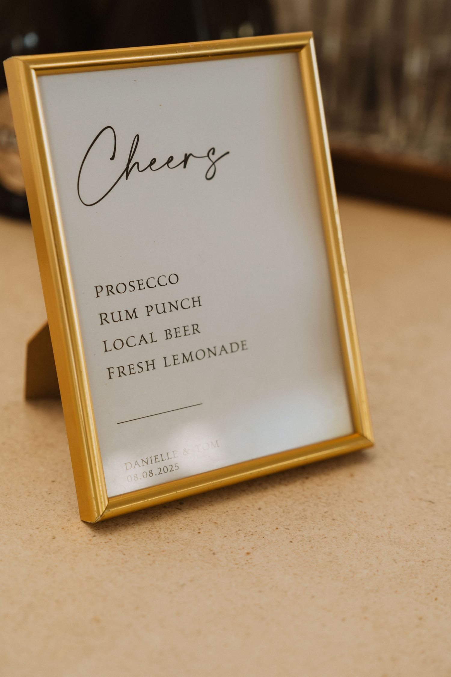Gold-framed drink menu signs displaying options like prosecco, rum punch, and fresh lemonade at an elegant event.