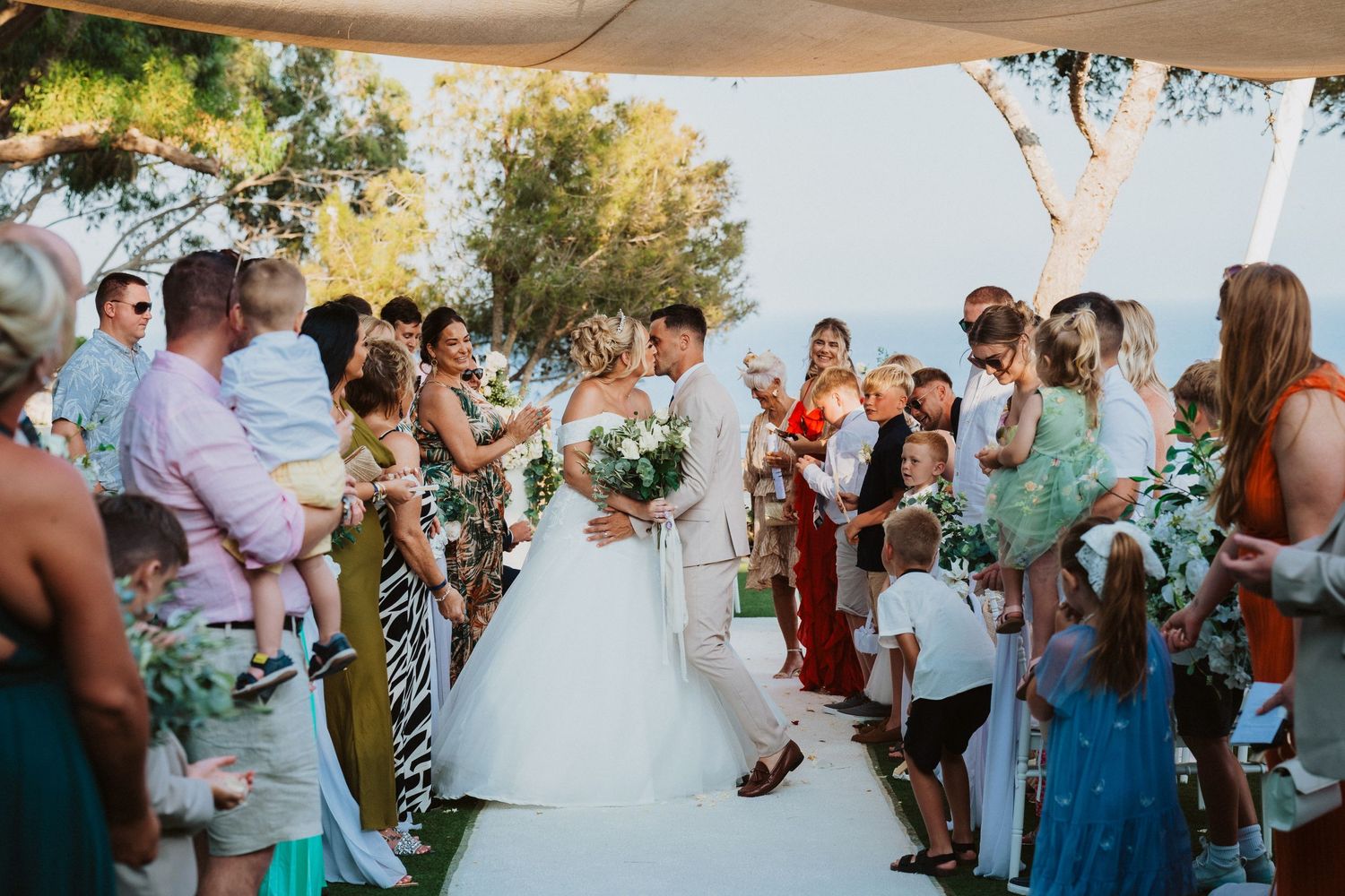 Wedding guests celebrate with confetti during an outdoor ceremony under shade sails.