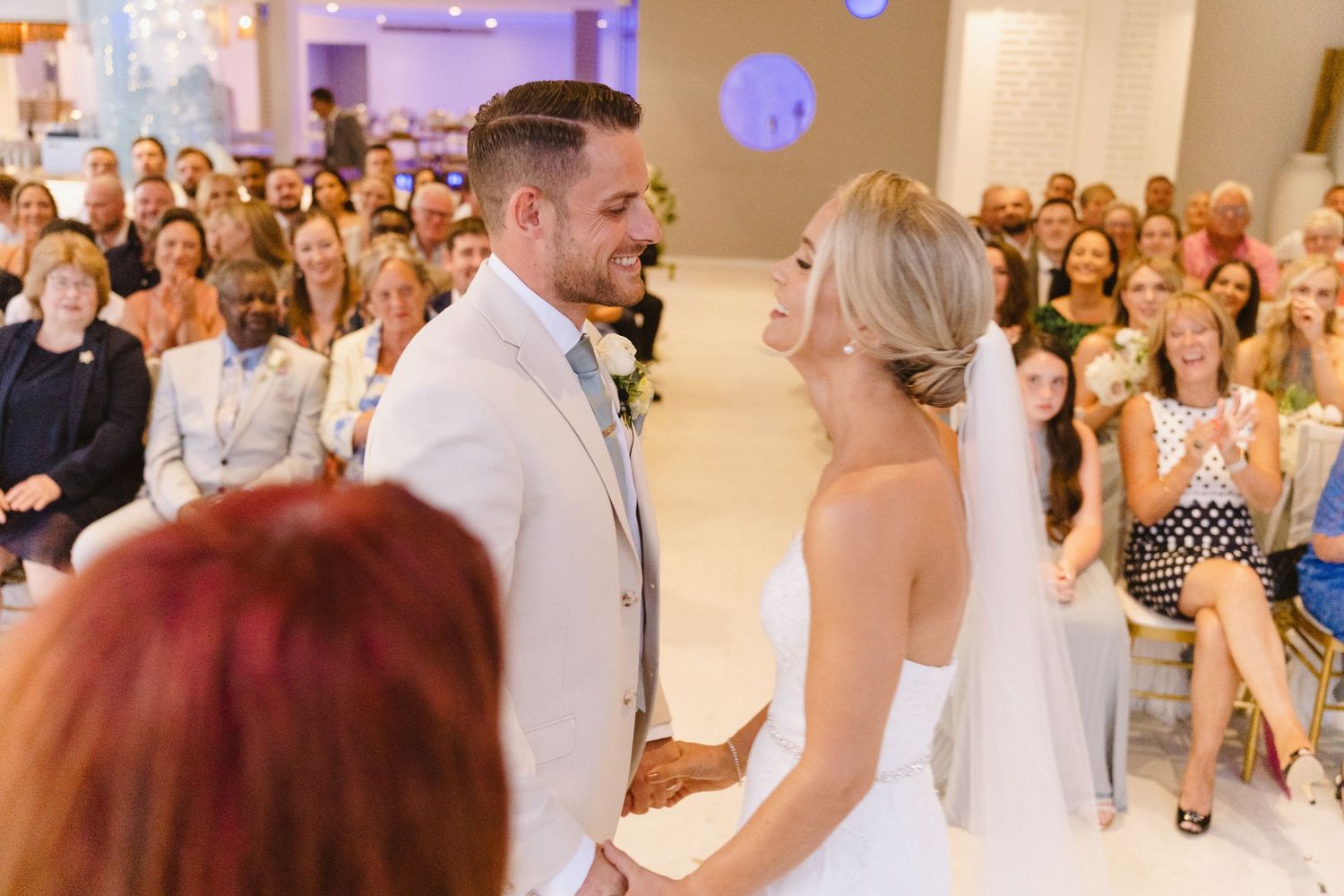 Wedding ceremony in a modern venue with white decor and purple ambient lighting.