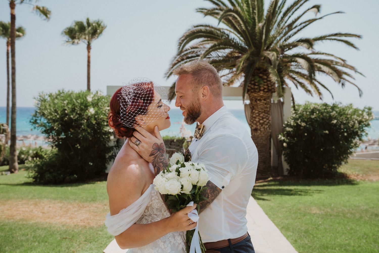 Romantic wedding portrait with couple embracing under palm trees by the ocean.