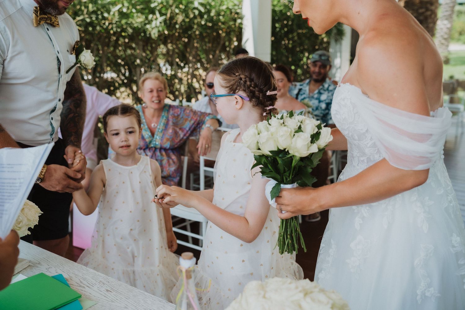A wedding celebration with young participants gathered around a white-decorated table outdoors.