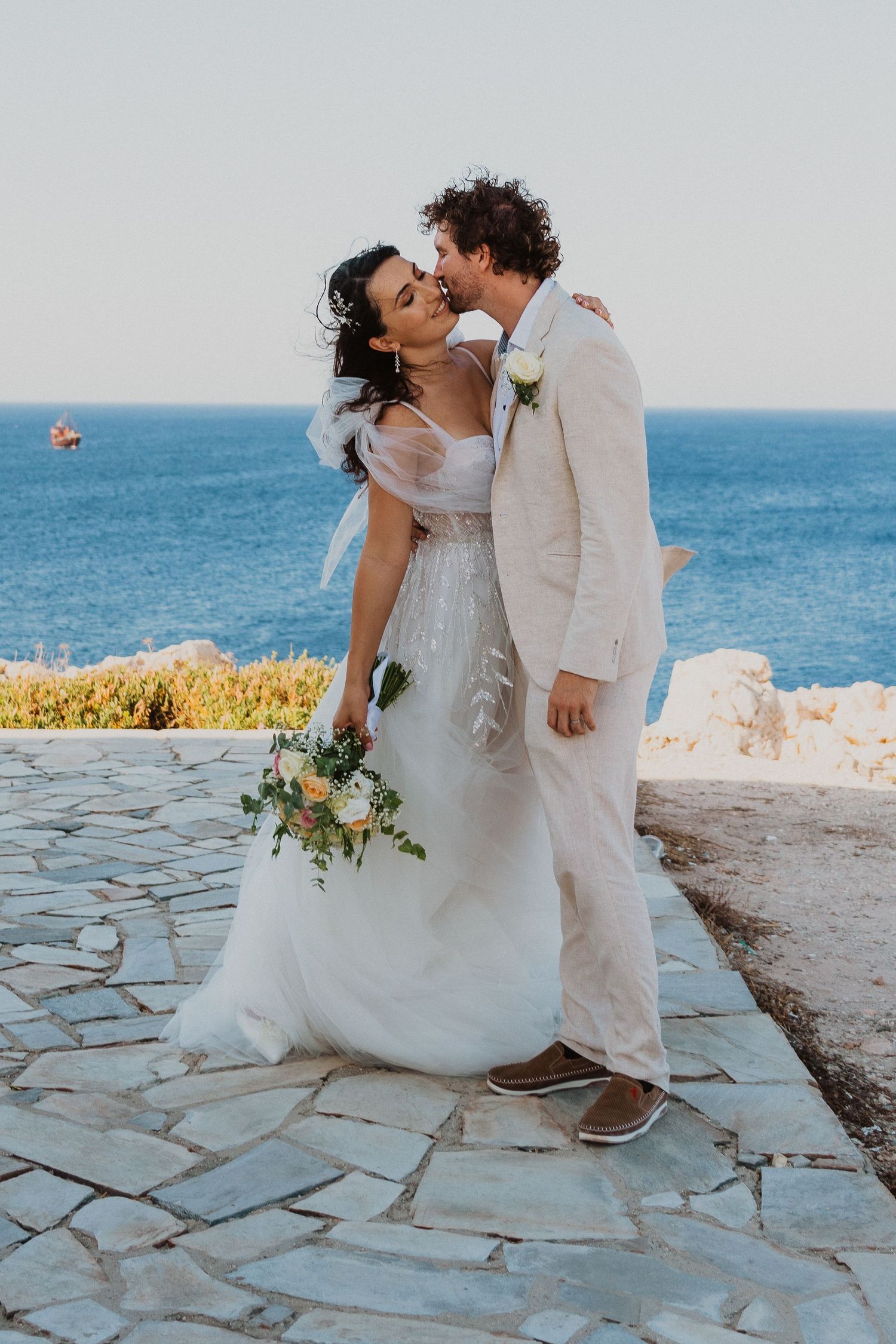 A couple shares a joyful moment at their seaside wedding ceremony on a stone terrace overlooking the blue ocean.