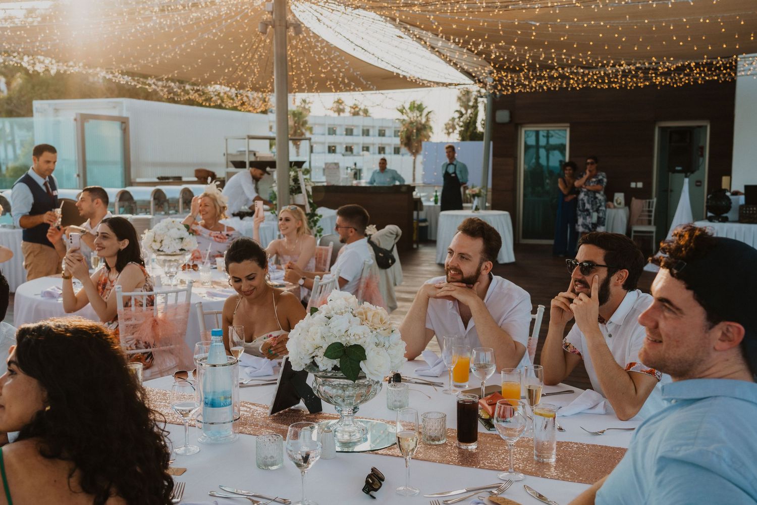 Sunset wedding reception with guests seated at tables under string lights.