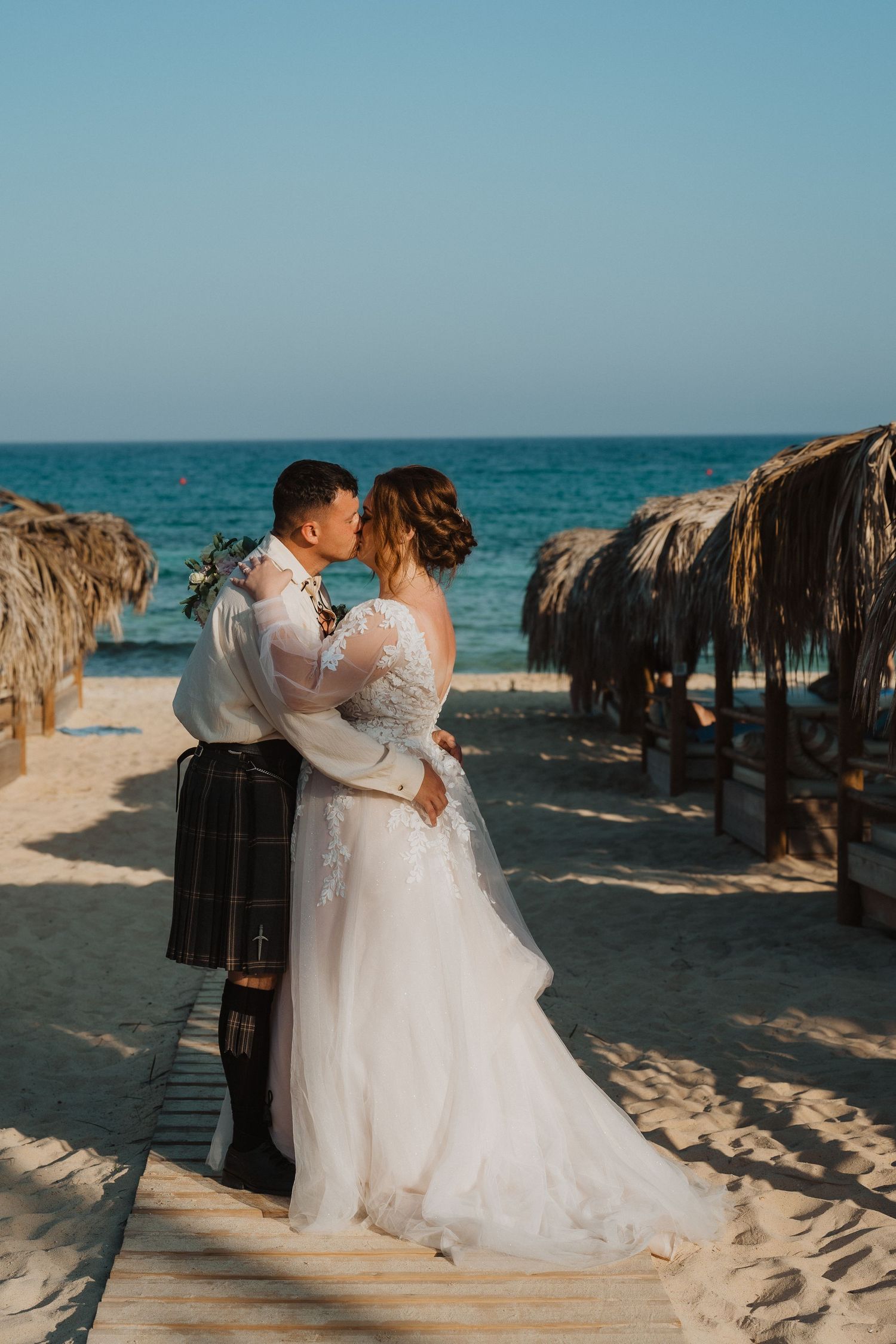 A romantic embrace on a beach boardwalk surrounded by thatched umbrellas and turquoise waters.