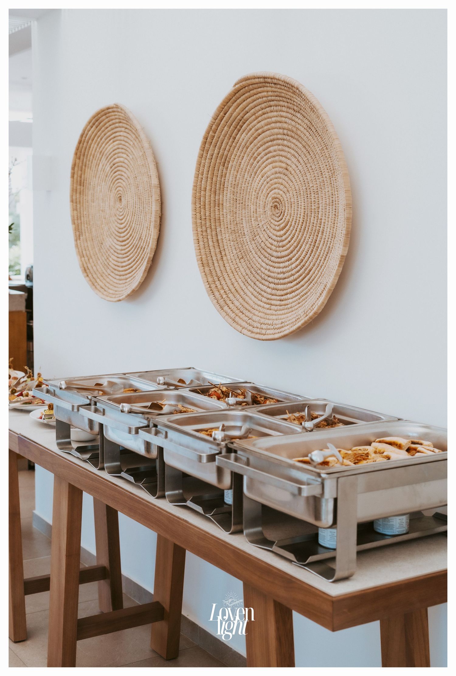 Catering setup with chafing dishes and woven wall decor at a wedding reception.
