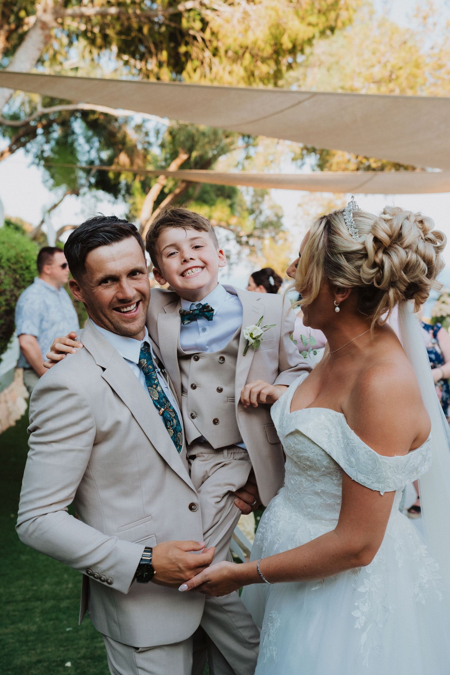 Joyful wedding moment with couple and young ring bearer under outdoor tent.