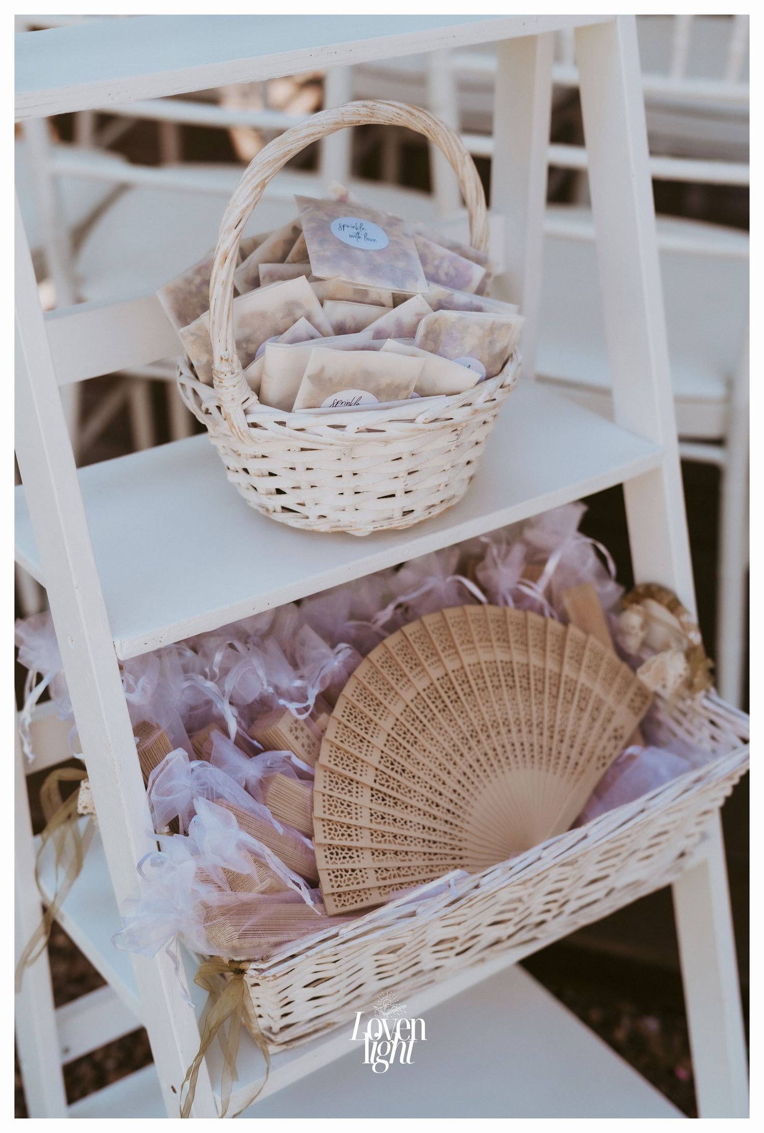 White woven baskets with delicate decorative elements and a wooden fan placed on a ladder shelf.