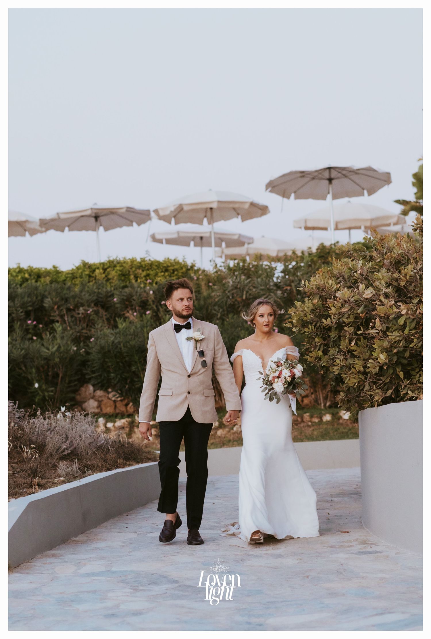 Elegant wedding couple walking beneath white umbrellas in an outdoor garden setting.