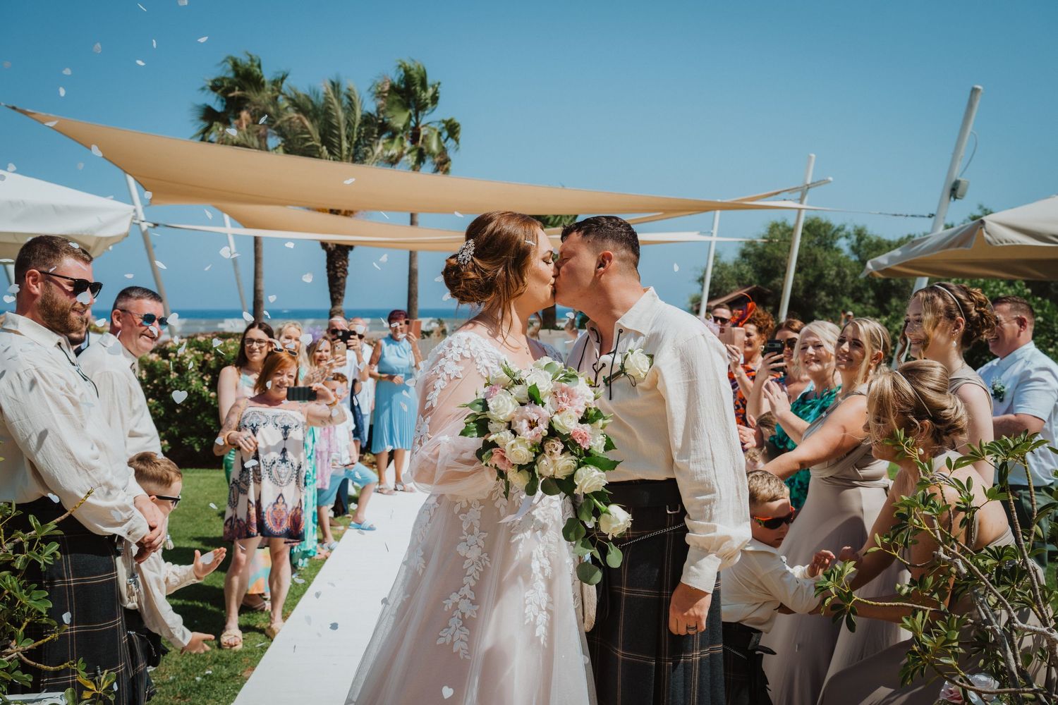 Wedding ceremony under cream-colored shade sails with guests gathered around celebrating the couple's special moment.