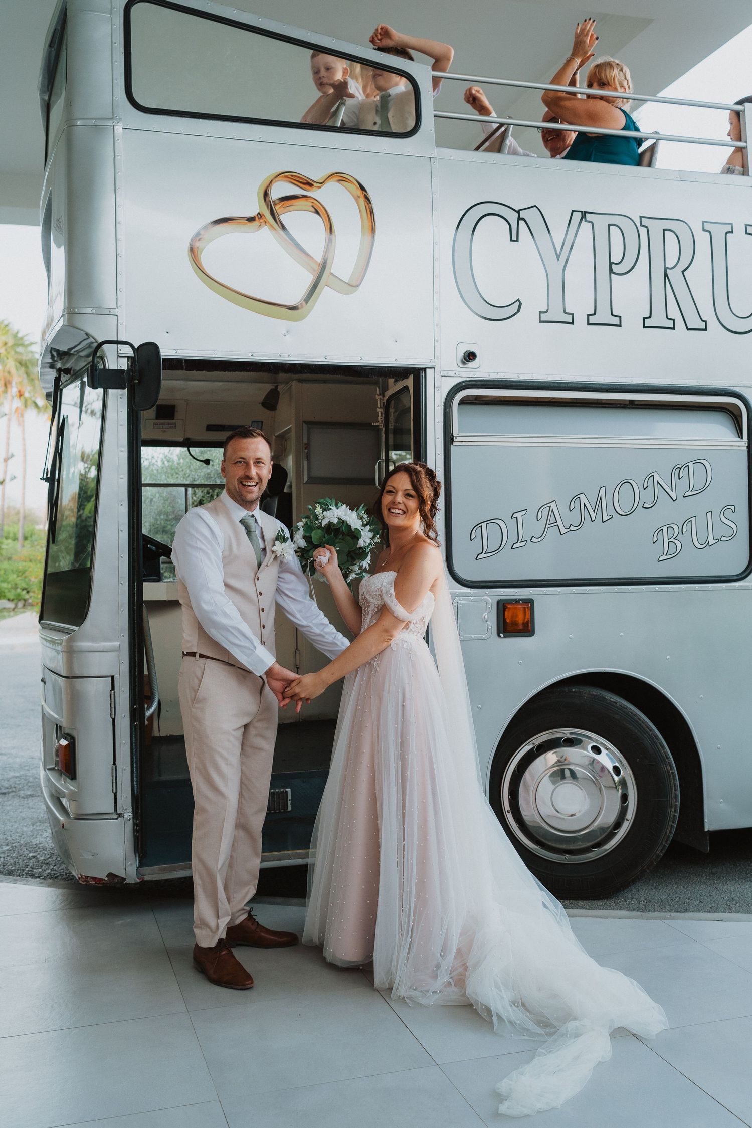A wedding couple poses in front of a Cyprus Diamond Tours bus decorated with gold heart decals.