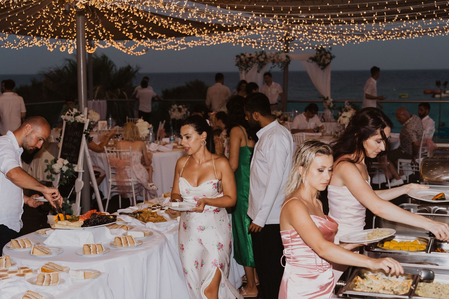Wedding guests serve themselves at an elegant outdoor buffet under twinkling lights.