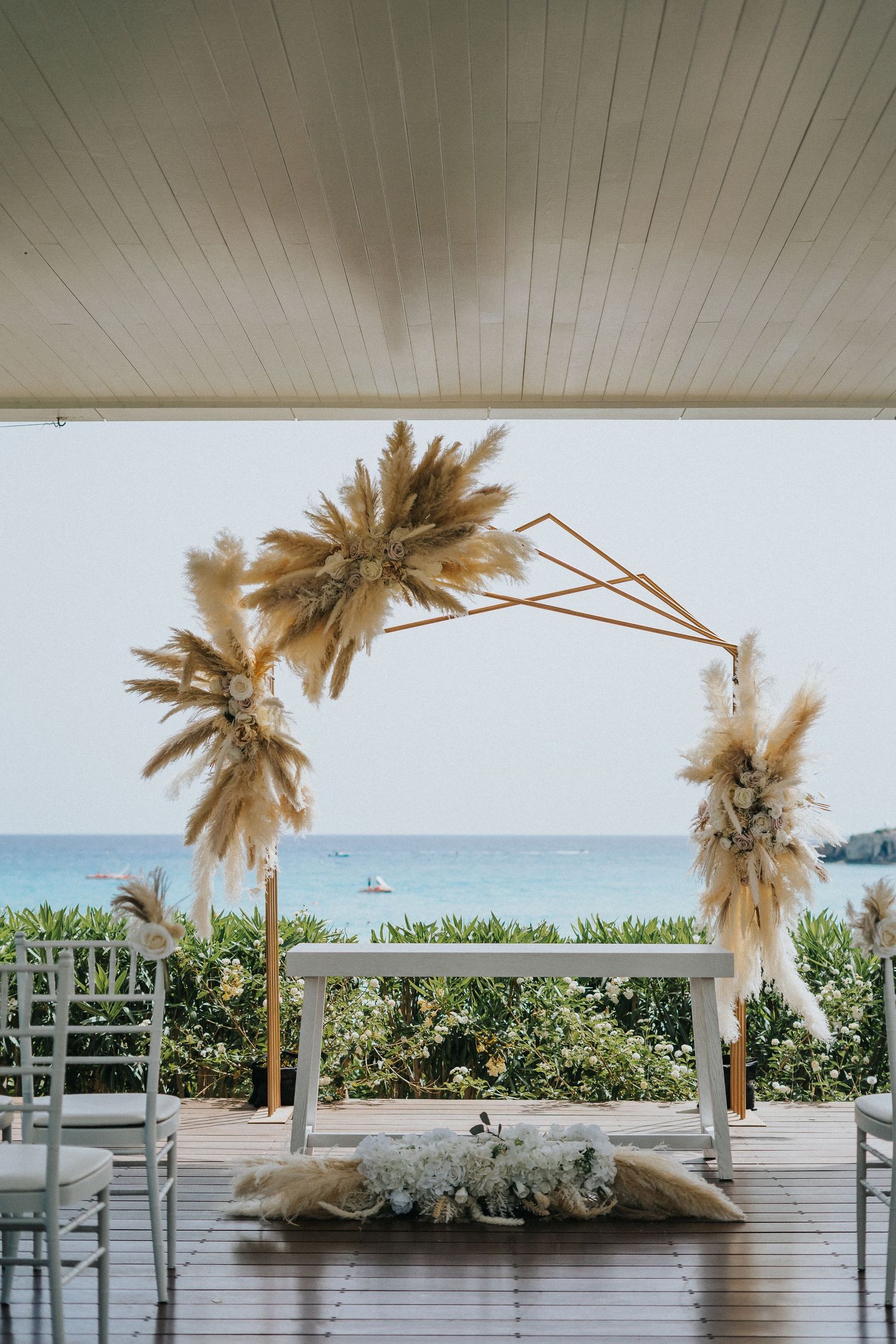 Beachfront wedding arch decorated with pampas grass and white flowers overlooking the ocean.