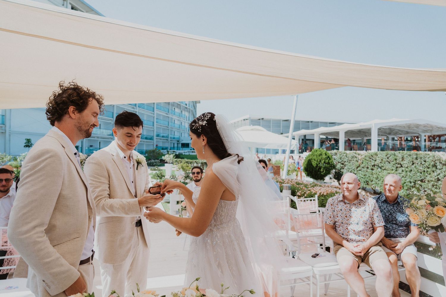 Wedding ceremony on a sunny deck with neutral decor and floral arrangements.