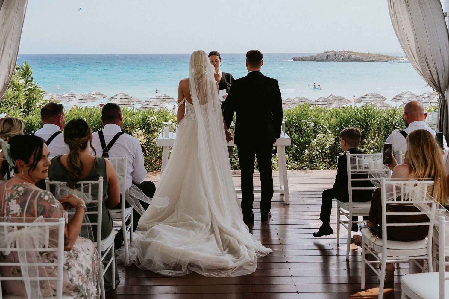 Wedding ceremony overlooking the ocean with white chairs and draped fabric.
