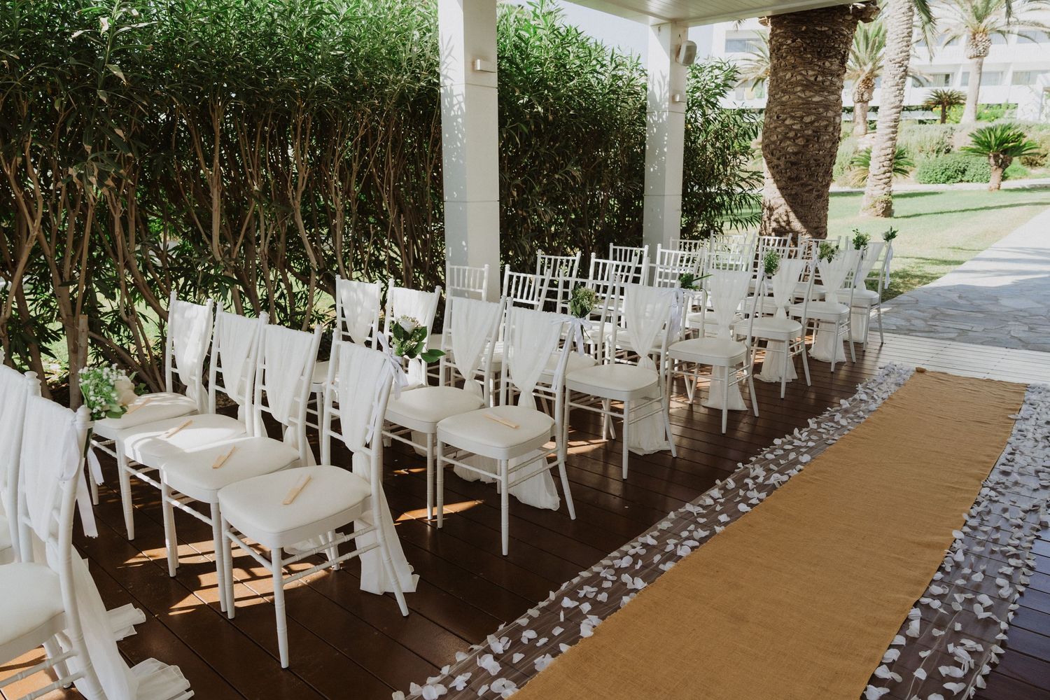 White ceremony chairs line a brown aisle runner with stone borders under a covered patio.