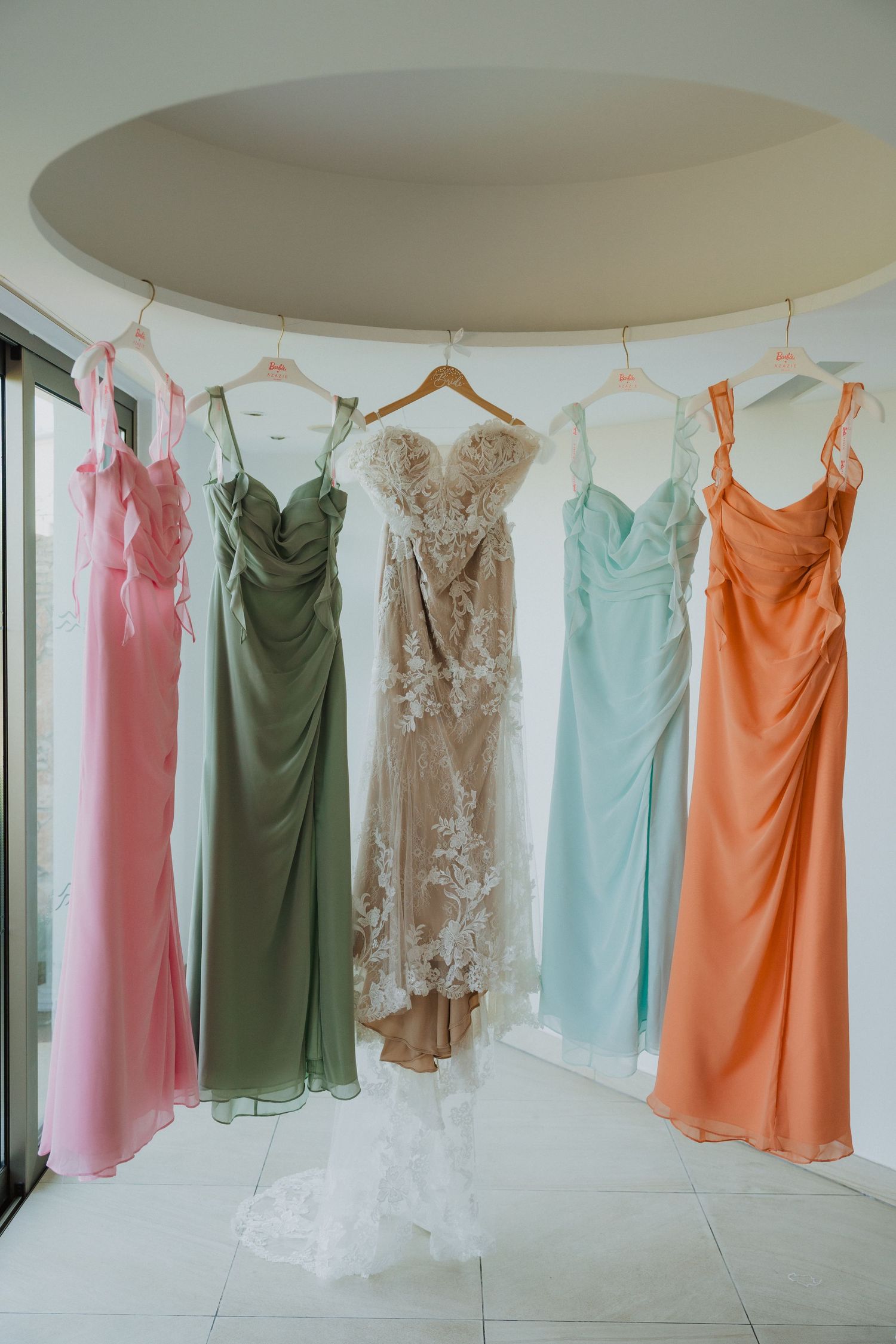 Colorful bridesmaid dresses in pink, green, blue and orange hanging on a clothing rack.