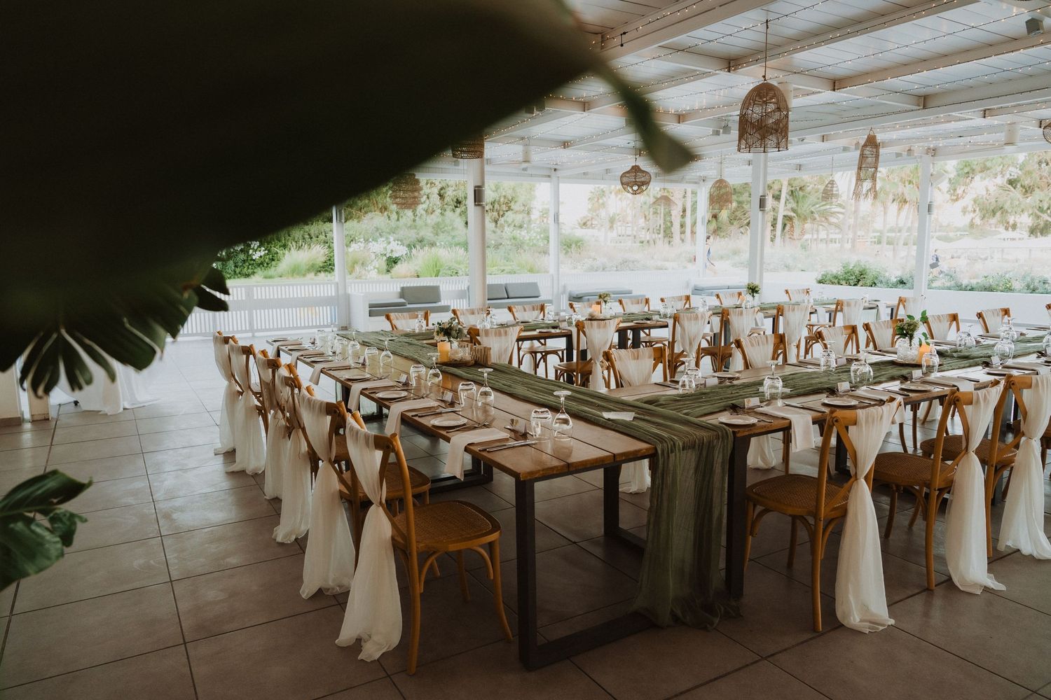 Wedding reception venue with long wooden tables and white-draped chairs under a covered patio.