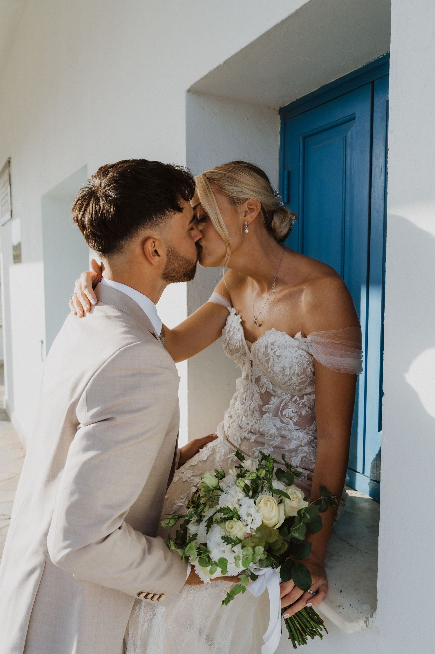 Romantic wedding couple embraces near bright blue doors in a Mediterranean setting.