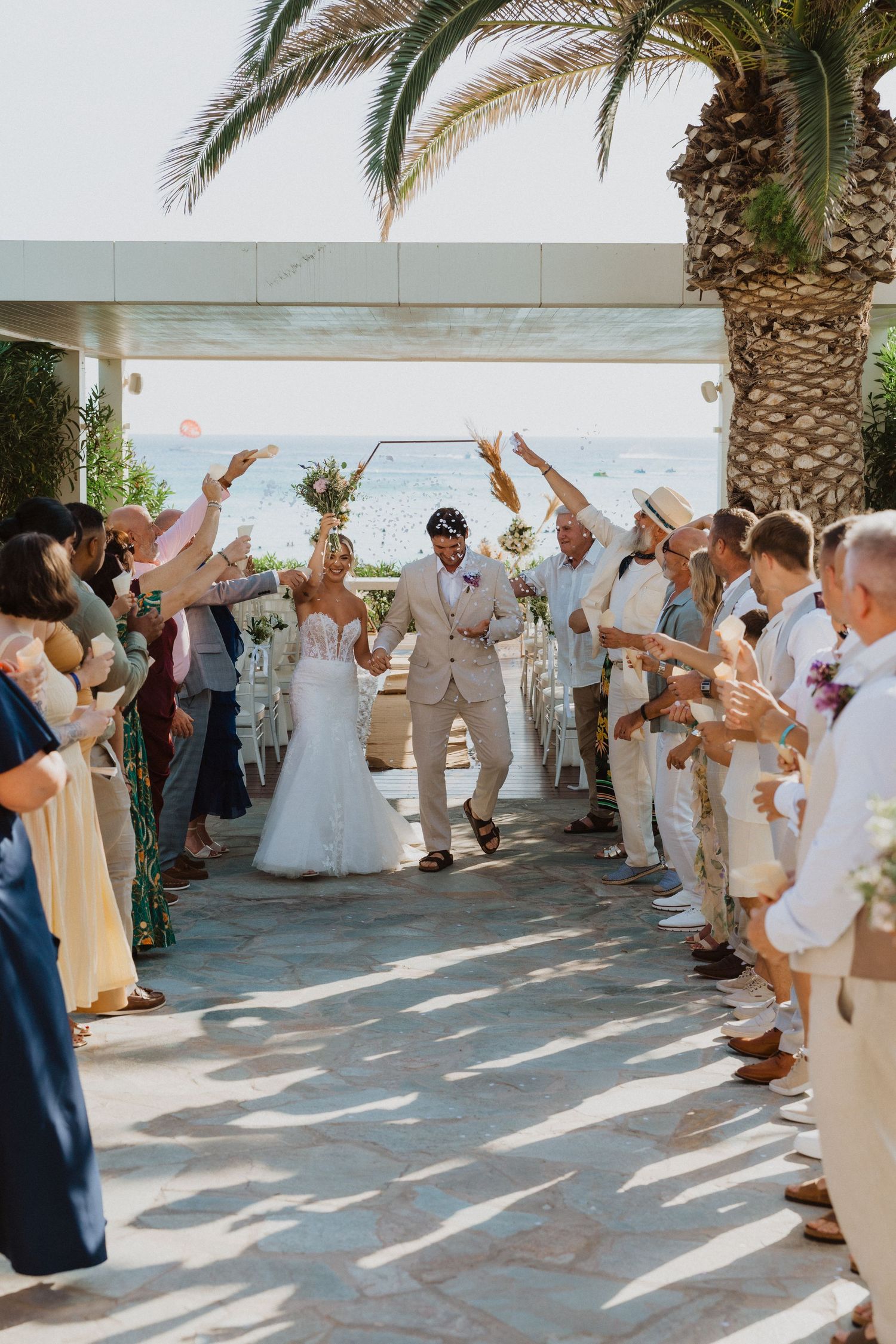 Wedding party and guests create a celebratory exit pathway at a beachside venue.