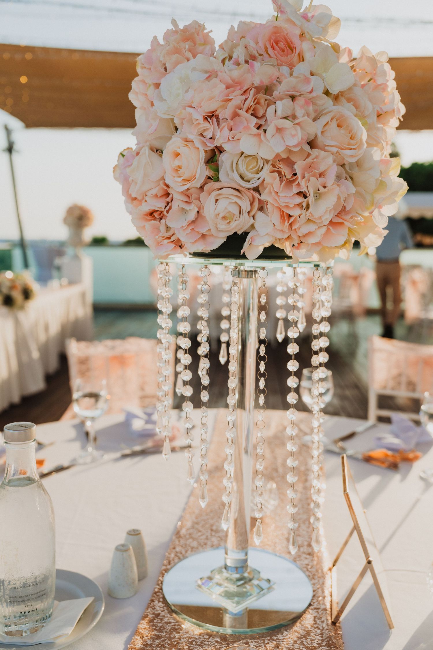 Crystal chandelier centerpiece with peach roses and hanging beads on white tablecloth.