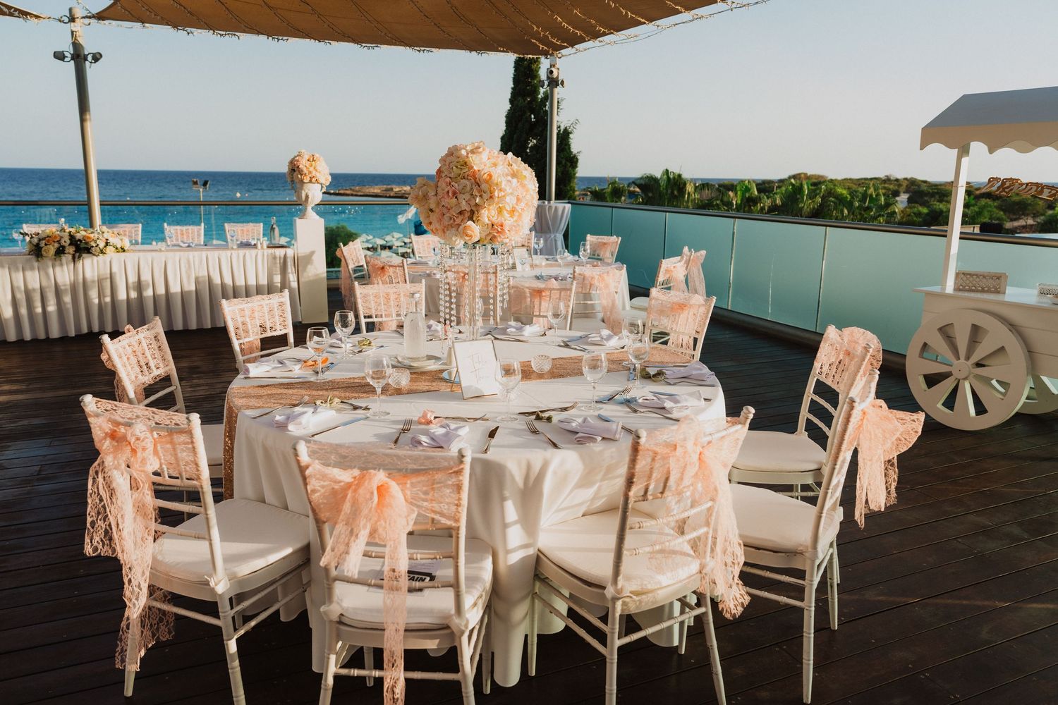 Elegant outdoor wedding reception setup with white tables and chairs overlooking the ocean.