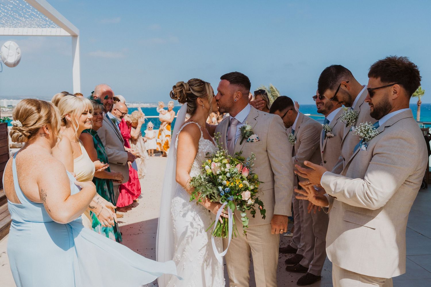 A sequence of wedding celebration photos showing couples kissing on a beach with guests in attendance.