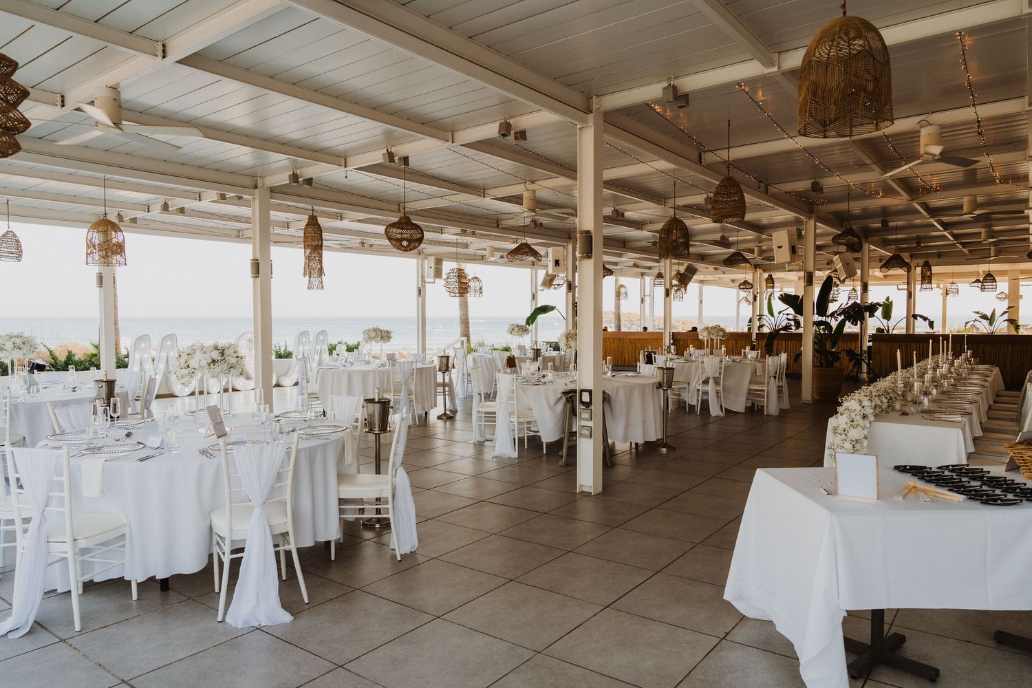 Panoramic view of an elegant white wedding reception venue with hanging lights and round tables.