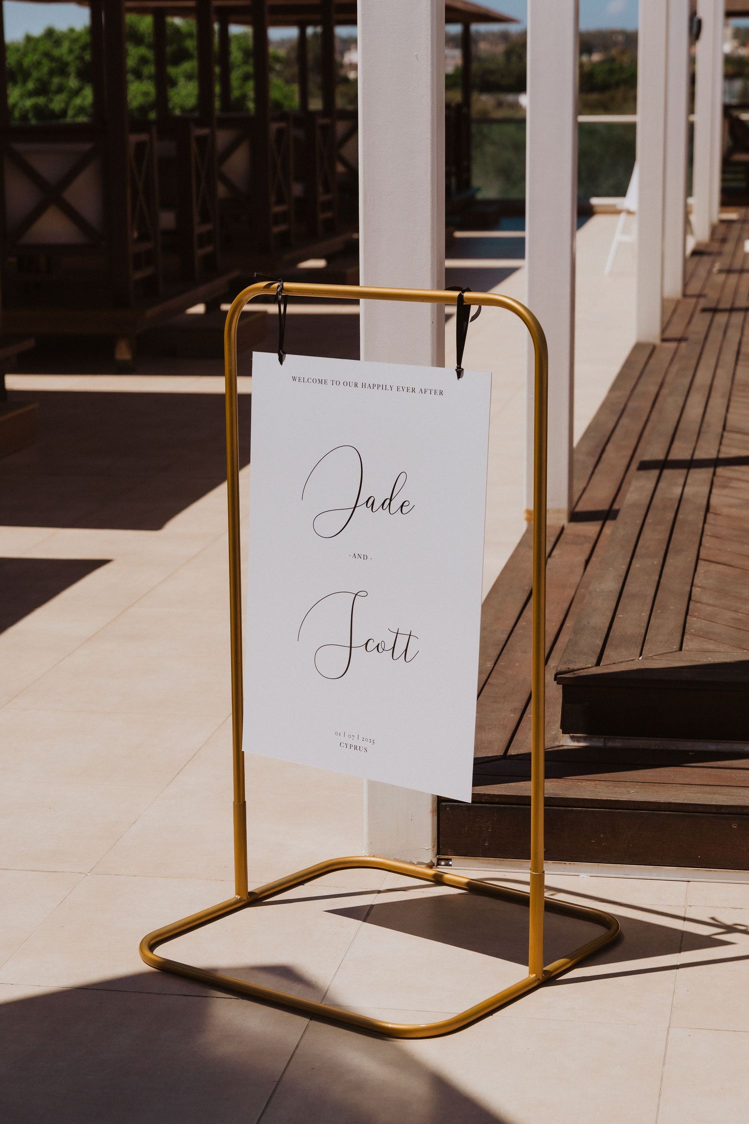 Elegant white place cards with calligraphy names displayed on gold metal stands casting shadows in sunlight.