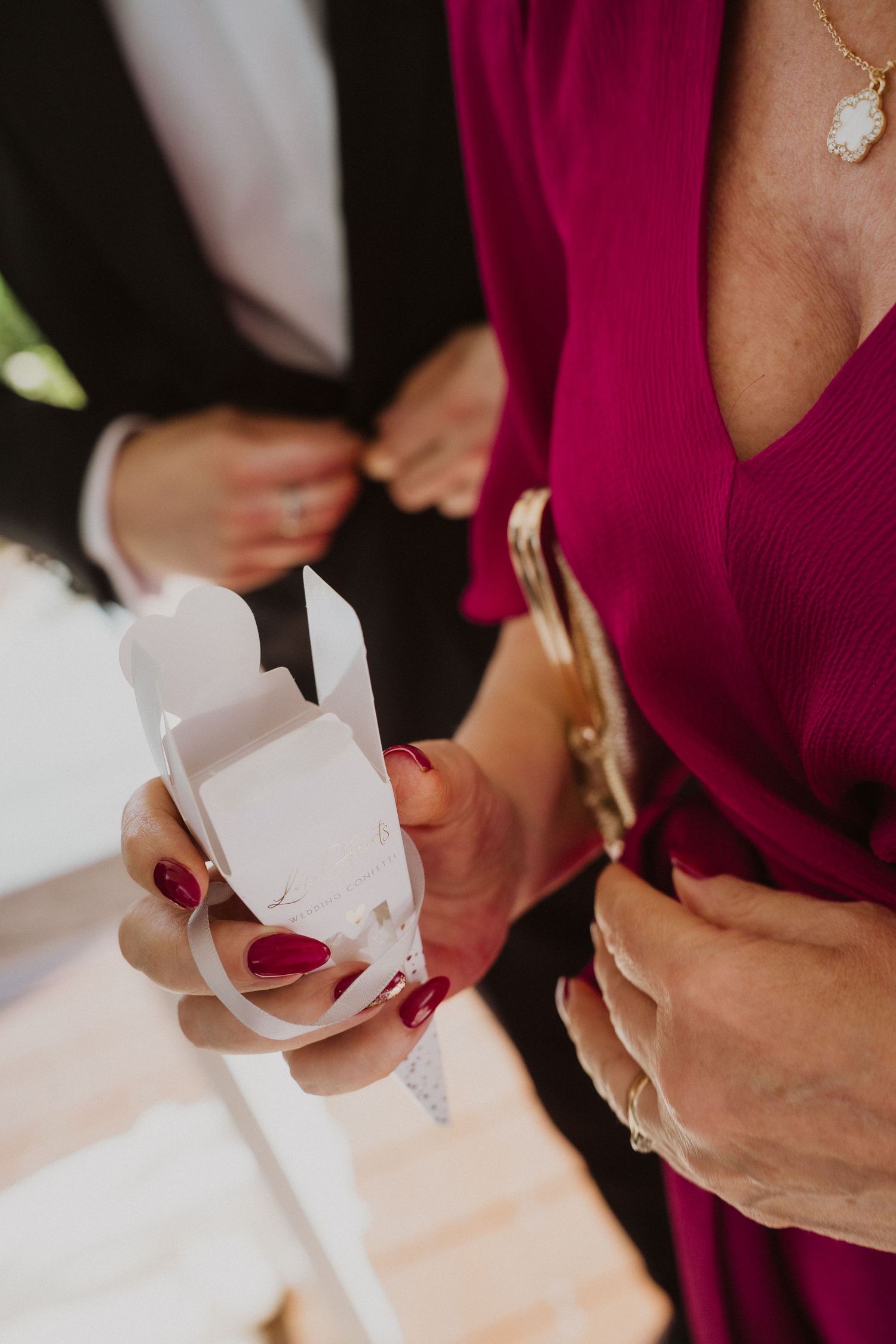 Close-up of a woman with red nails holding a white wedding favor box at an elegant wedding celebration.