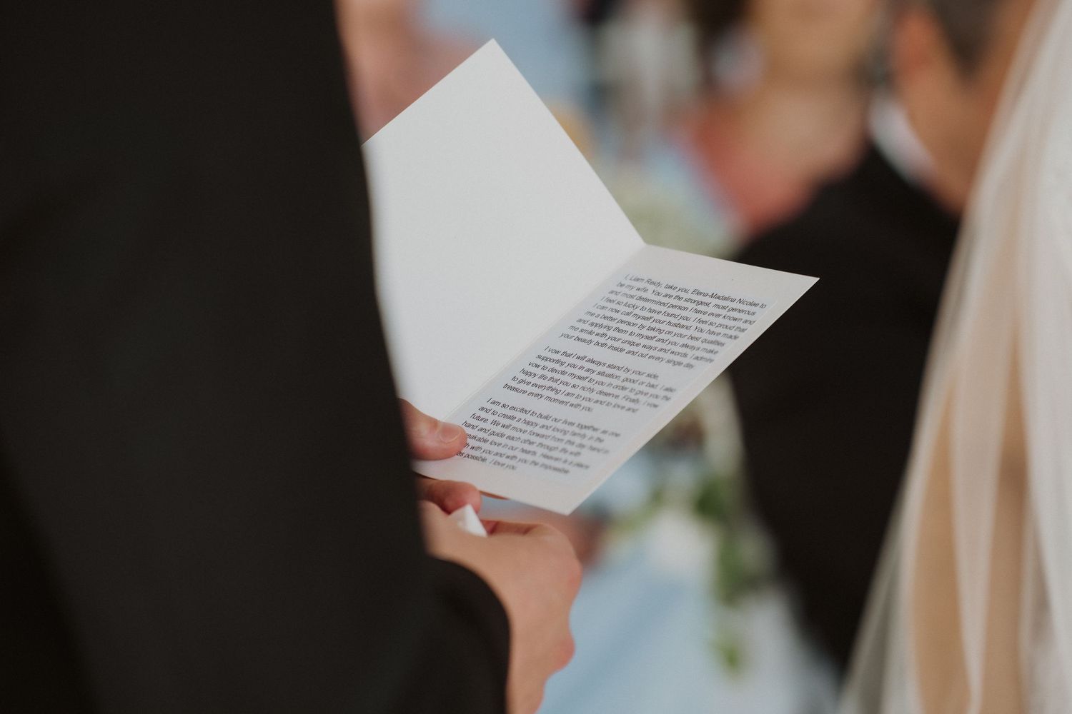 Close-up of groom holding wedding vow booklet during outdoor ceremony.