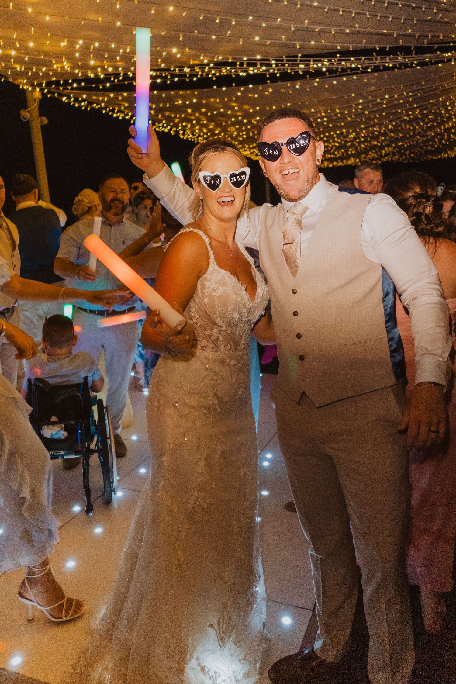 Wedding party dancing and celebrating under a canopy of twinkling string lights at an evening reception.