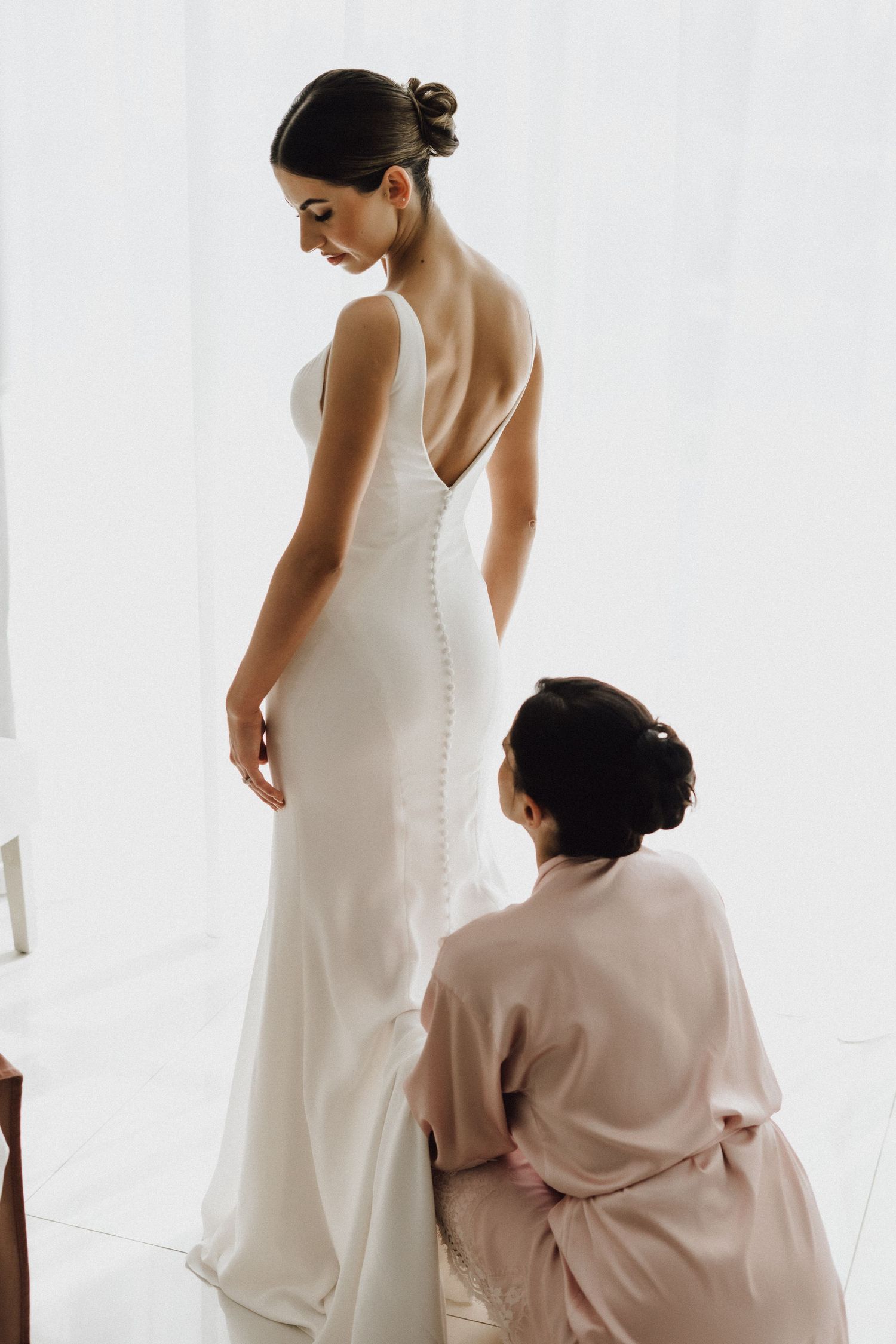 Elegant white wedding dress with deep v-back being fitted in bright studio setting.