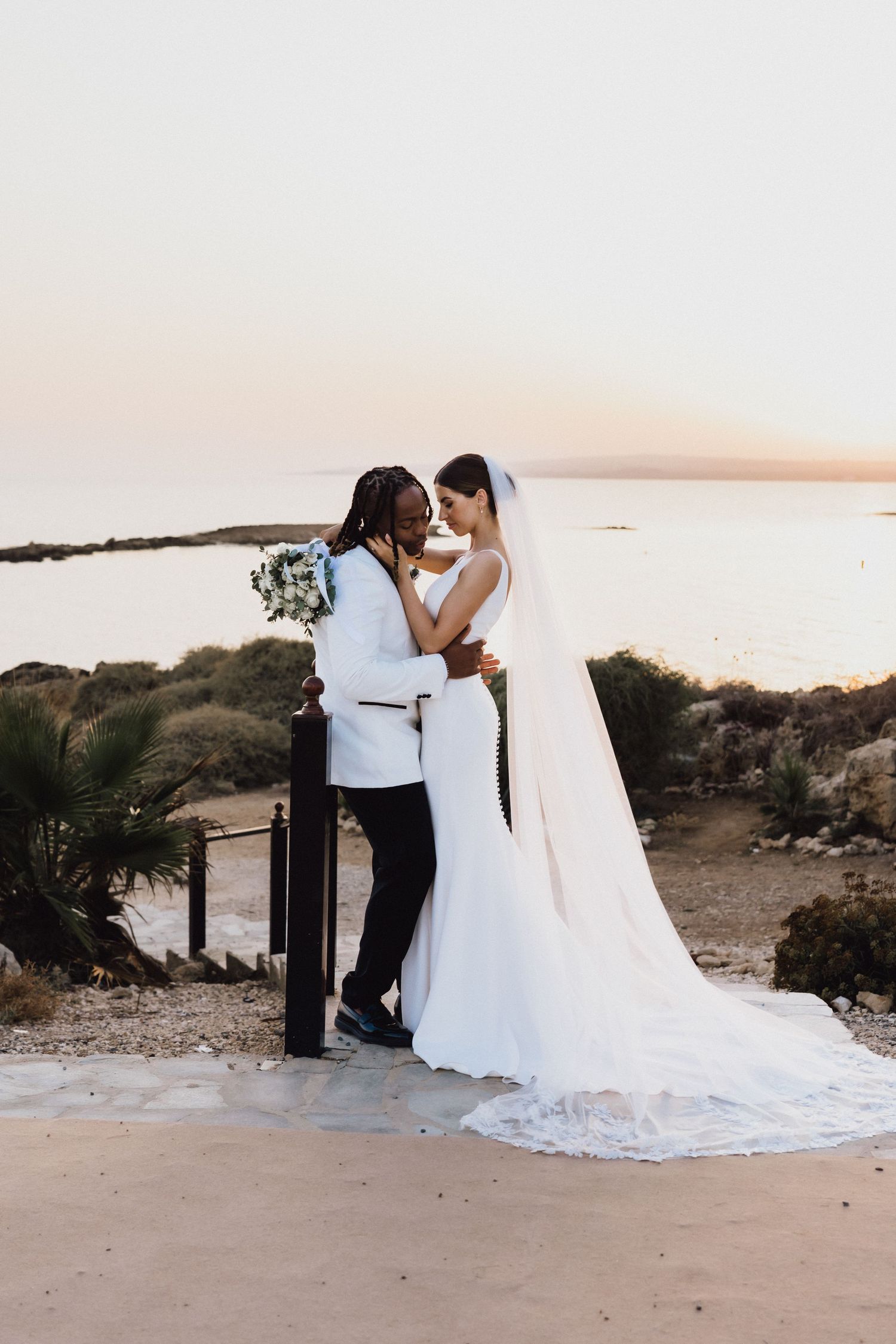 Intimate wedding moment captured against sunset coastal backdrop.