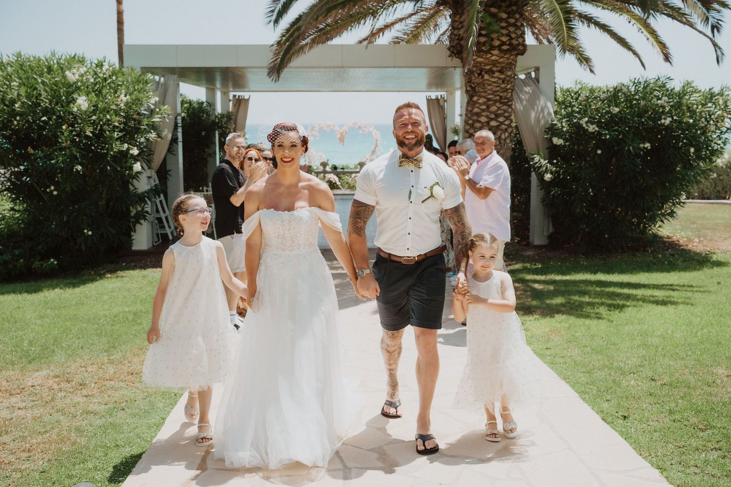 Beachside wedding party strolls along a sunny garden pathway.
